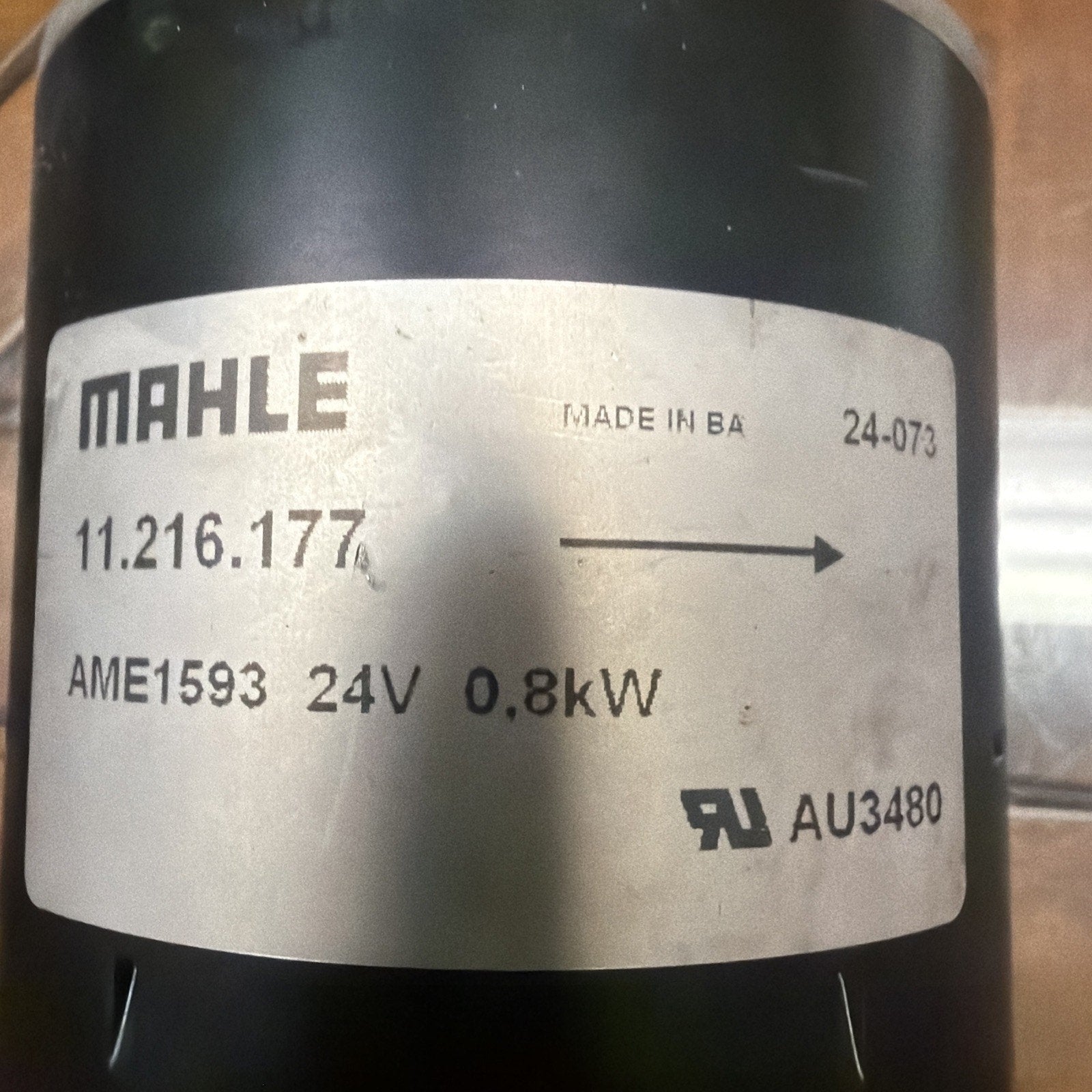White rectangular label with black printed text showing brand name "MAHLE," model number "11.216.177," voltage "24V," power rating "0.8kW," certification marks, and an arrow pointing right, affixed to a black cylindrical object.