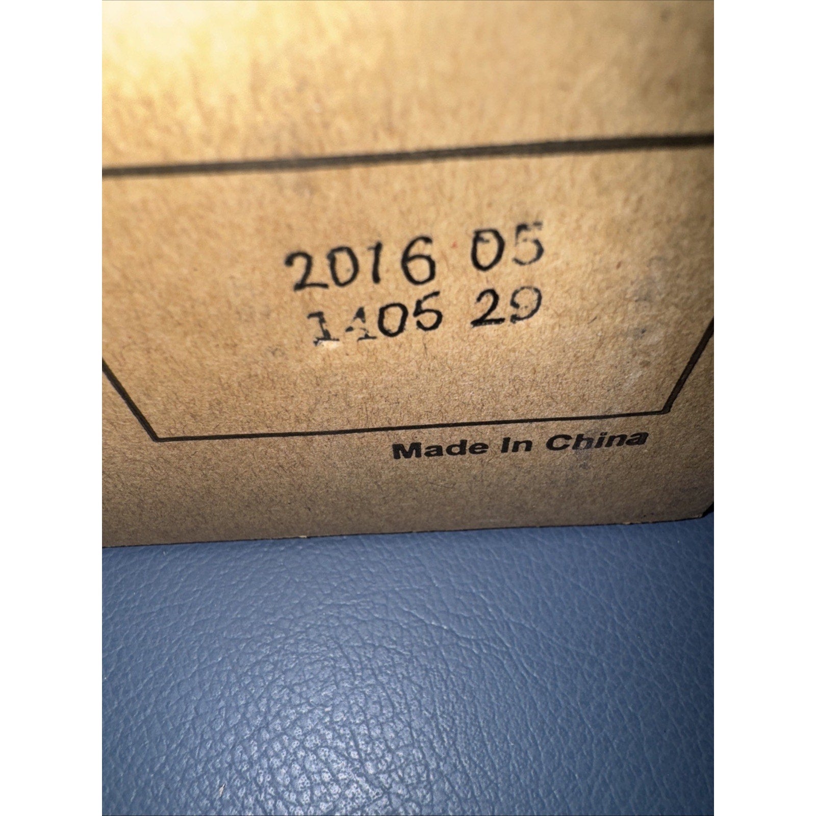 Close-up of a brown cardboard box corner with printed production date information and "Made In China" text on a blue textured surface background.