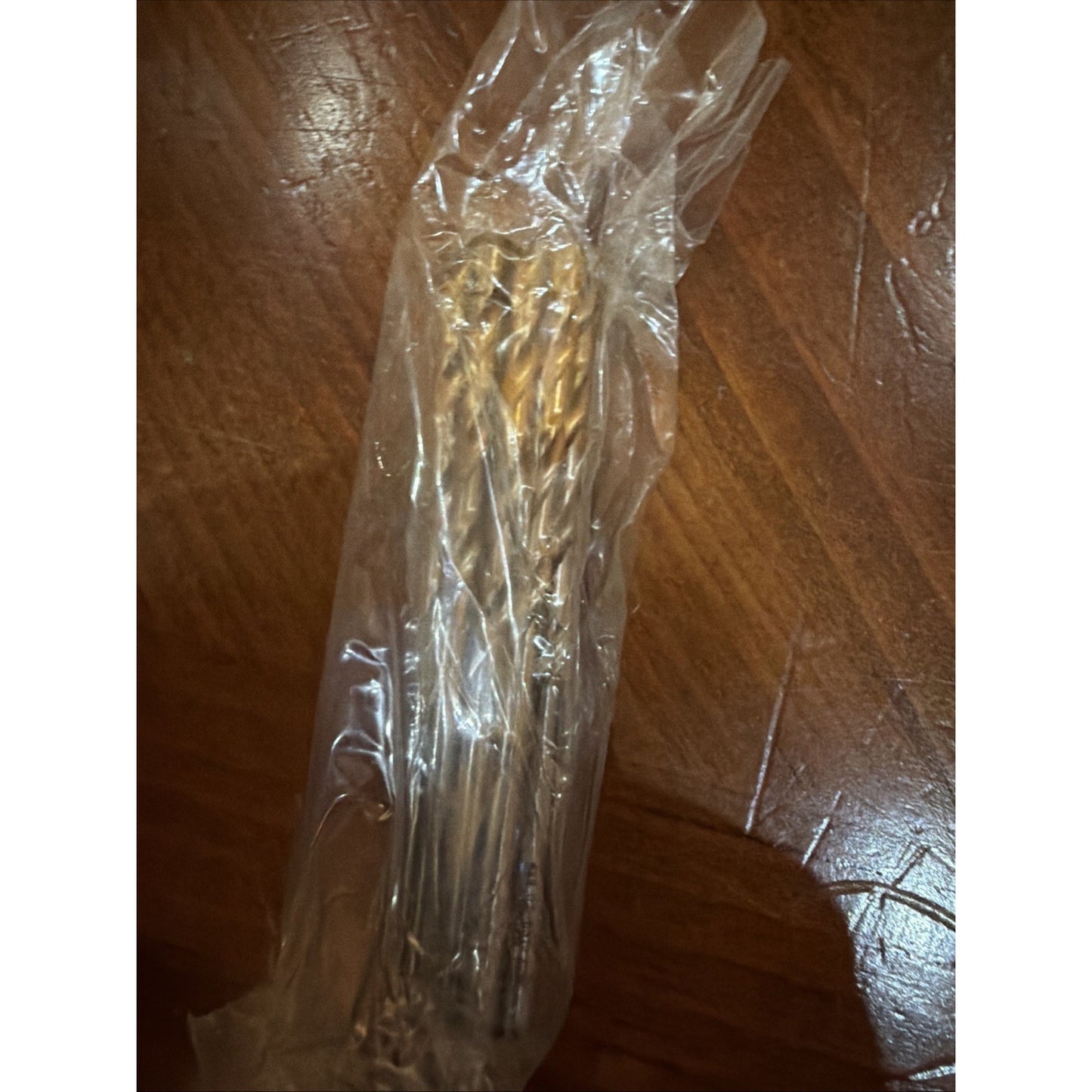 A set of several metal twist drill bits with golden-colored tips enclosed in clear plastic packaging, placed on a polished wooden surface.
