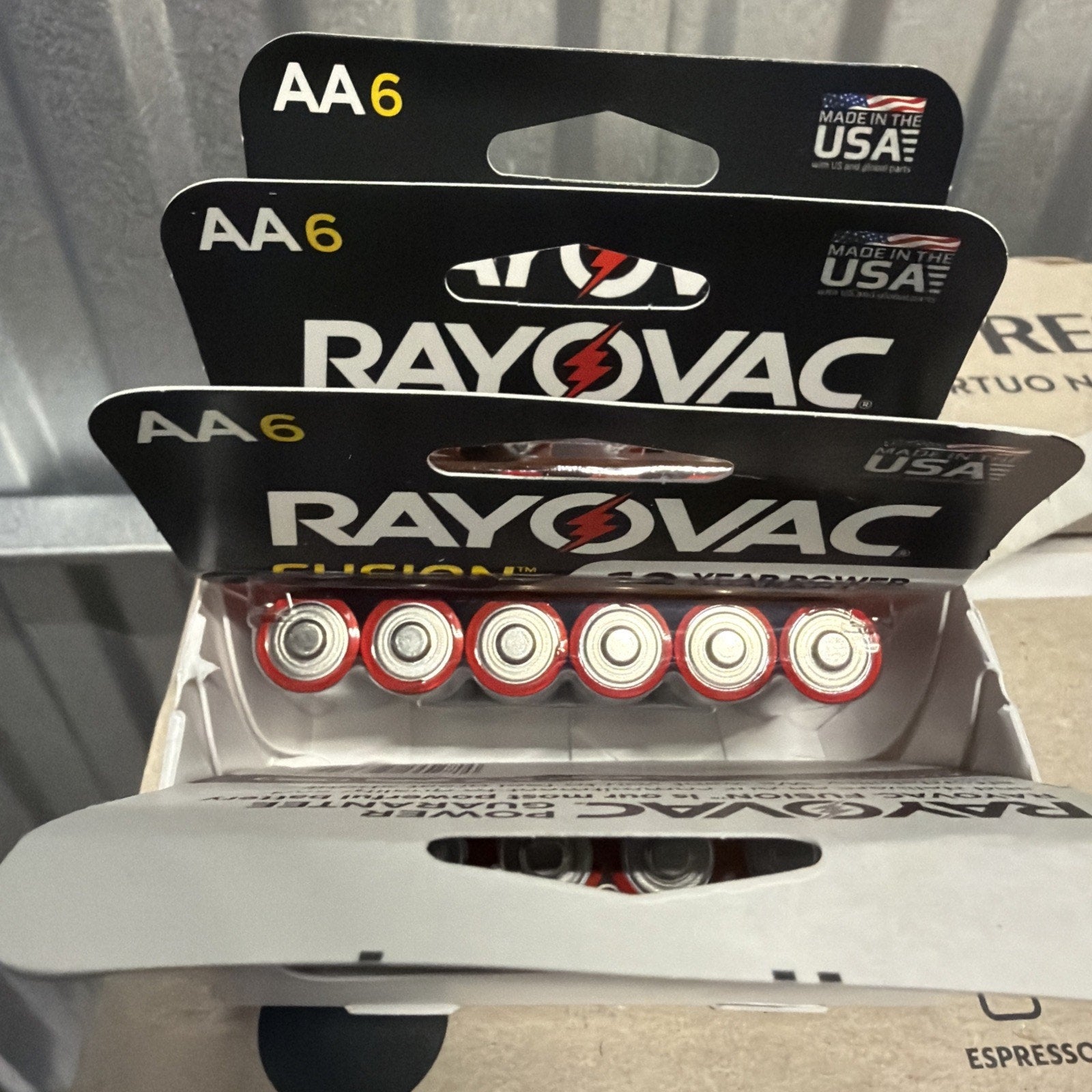 Open package showing three black and red boxes of Rayovac AA size batteries, each containing six batteries arranged in a row with visible positive terminals.