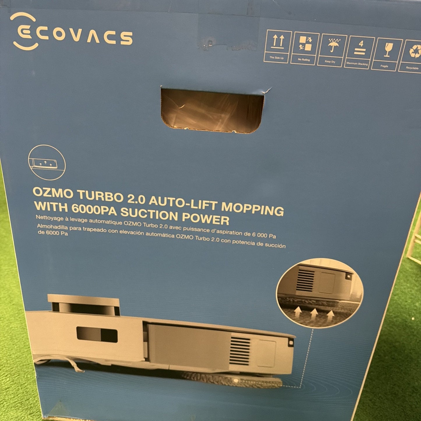 Blue packaging box featuring a side view image of a robotic vacuum with auto-lift mopping and 6000Pa suction power, branded with the Ecovacs logo and care icons.