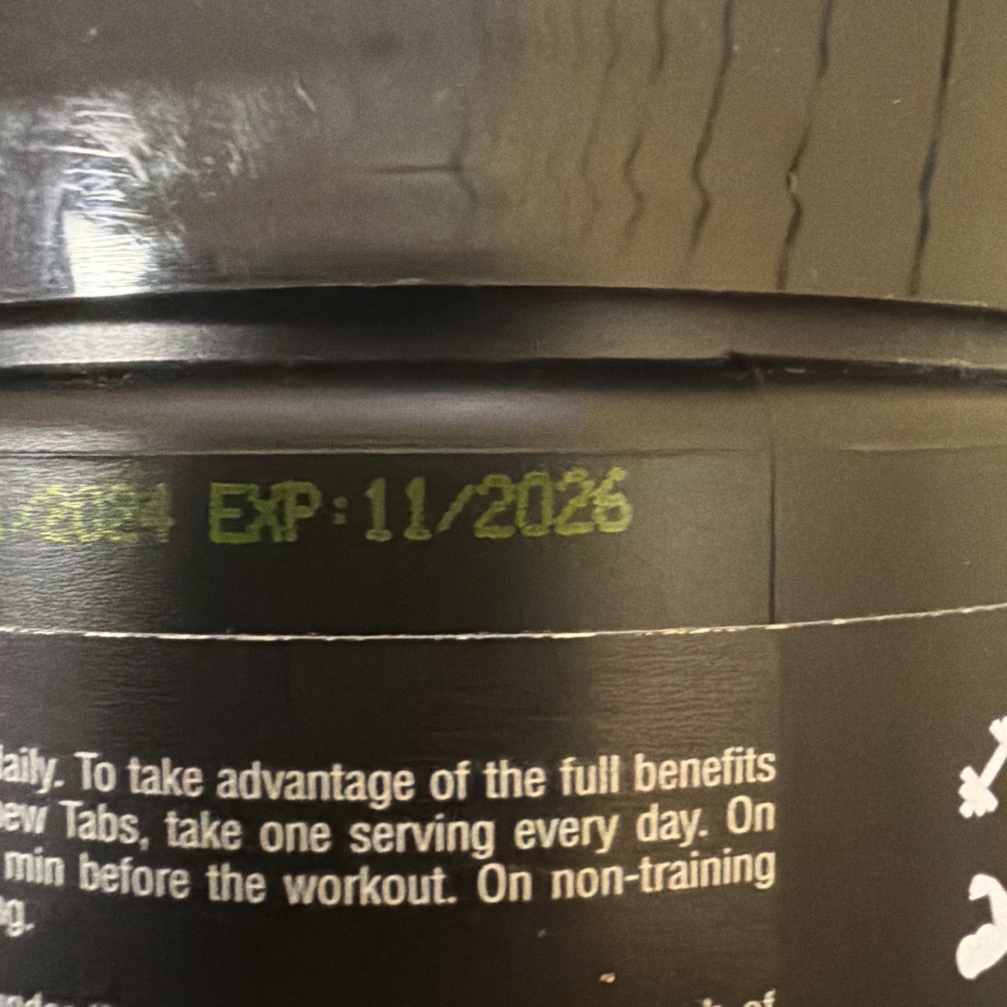 Close-up of an expiration date printed in yellow ink on a black plastic container, showing "EXP: 11/2026," above partially visible white text with usage instructions.