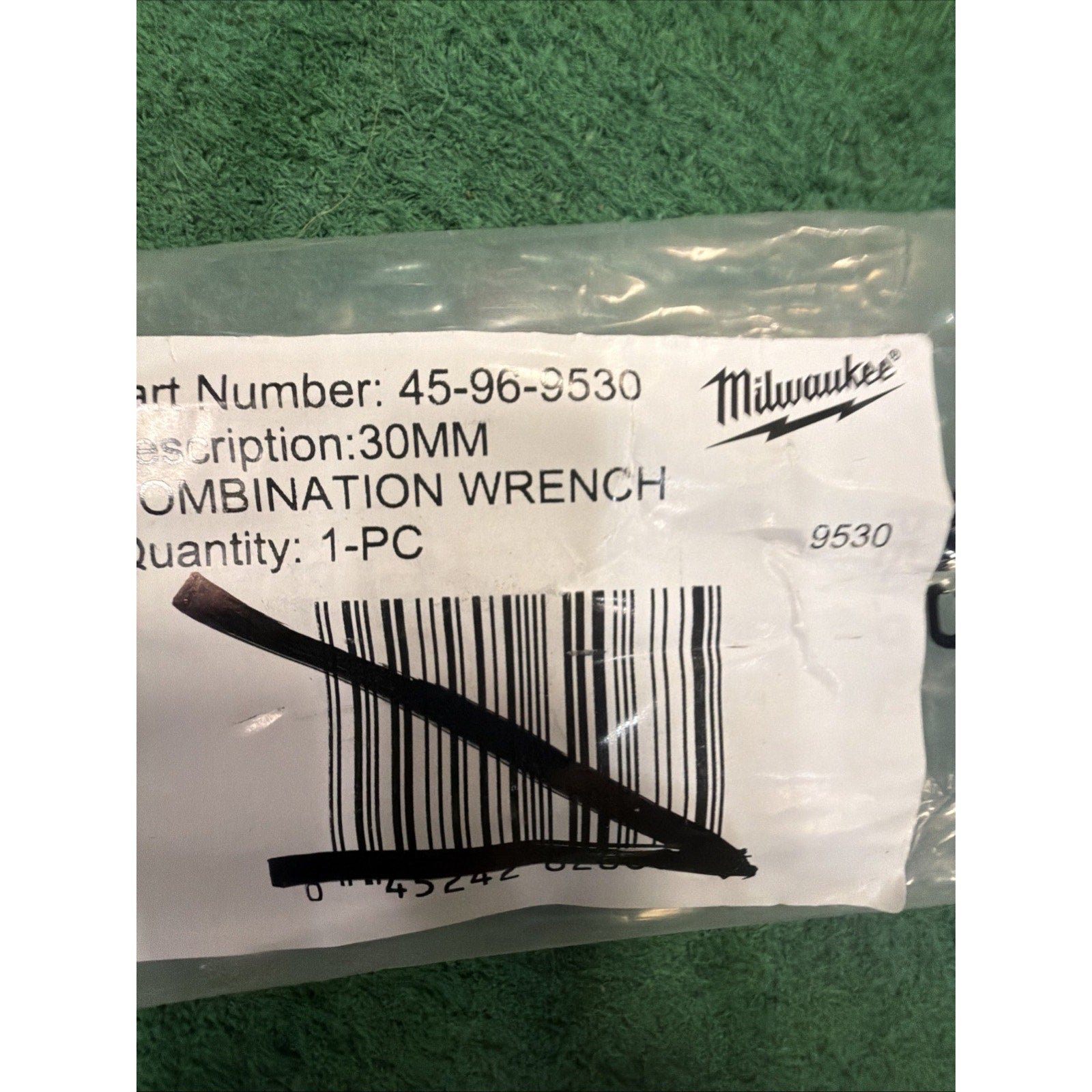 Clear plastic bag containing a label with printed part number, product description "30MM Combination Wrench," quantity "1-PC," and Milwaukee branding on a green textured background.