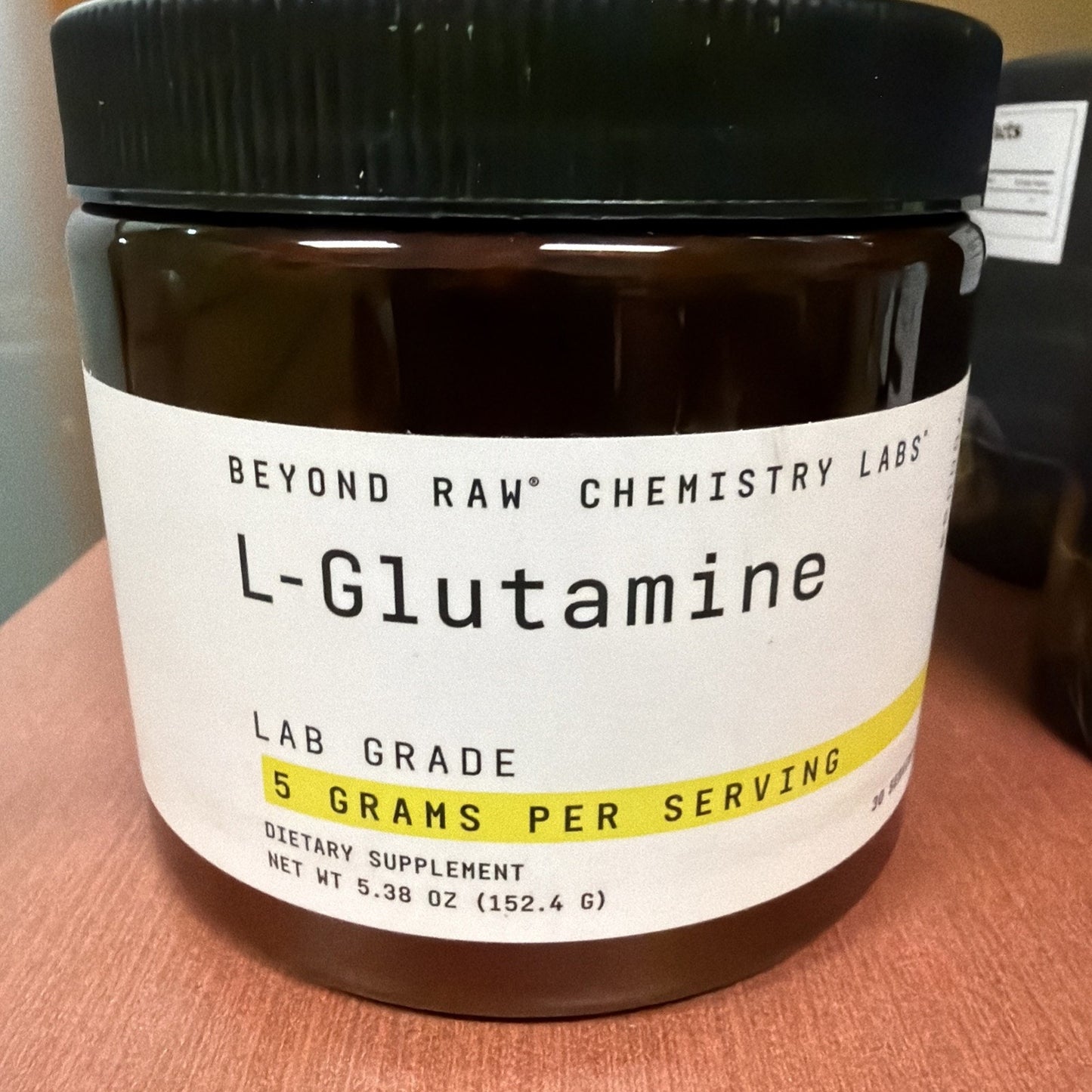 Dark brown container of Beyond Raw Chemistry Labs L-Glutamine dietary supplement with a white label highlighting 5 grams per serving and net weight of 152.4 grams.