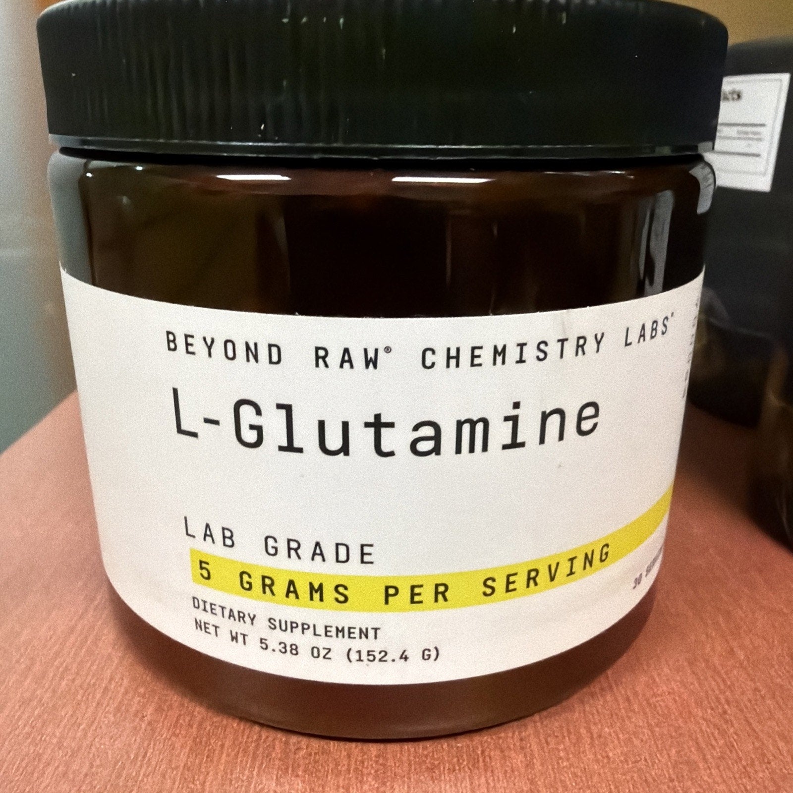 Dark brown container of Beyond Raw Chemistry Labs L-Glutamine dietary supplement with a white label highlighting 5 grams per serving and net weight of 152.4 grams.