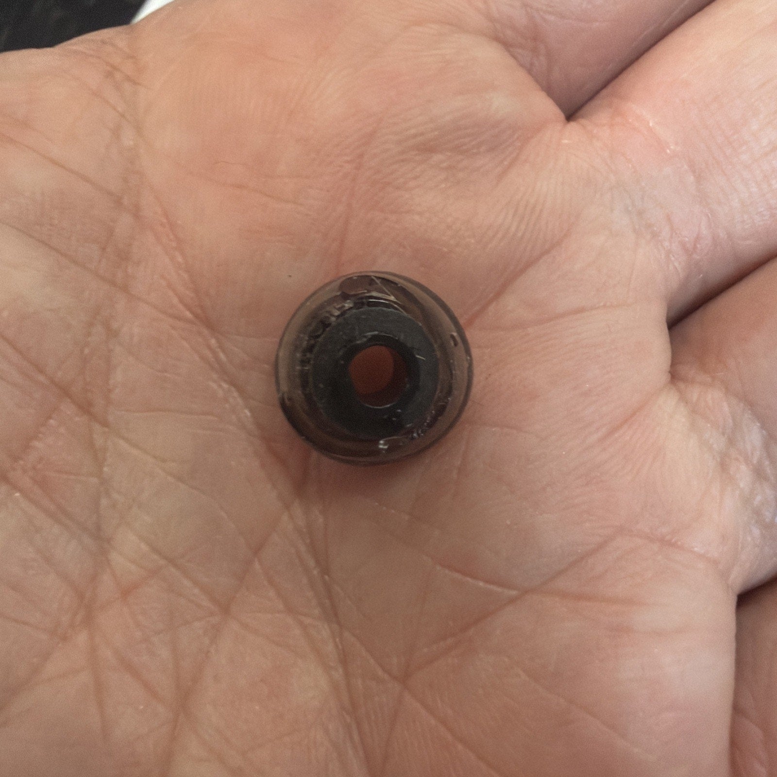 Close-up of a hand holding a small, round, translucent brown bead with a central hole, resting on the palm.