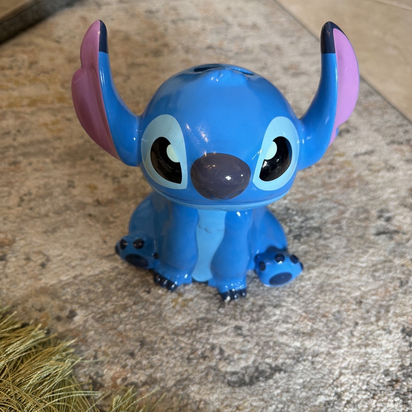 Blue ceramic figure of a cartoon character with large ears, black eyes, and a rounded nose, sitting on a stone surface with visible reflections on its glossy finish.