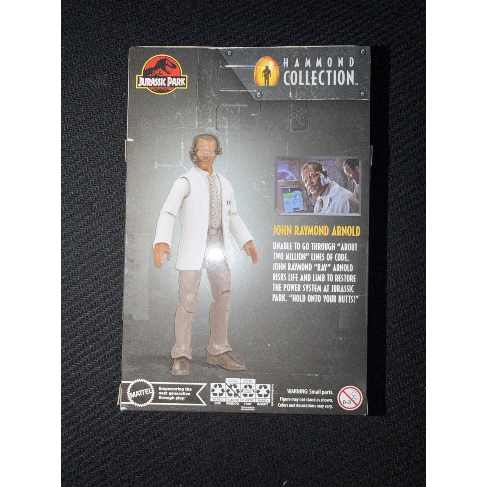 Back of a Jurassic Park Hammond Collection action figure packaging featuring John Raymond Arnold in a white lab coat, with a character description and a small scene image.