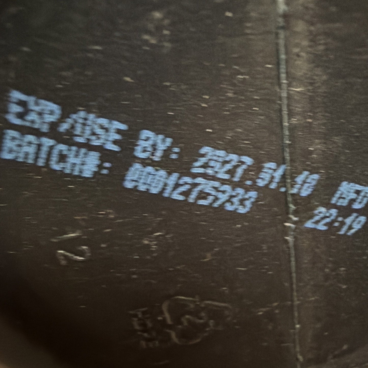 Close-up of a product's dark surface showing a white printed expiration date of 2027.01.10 and batch number 000127533.
