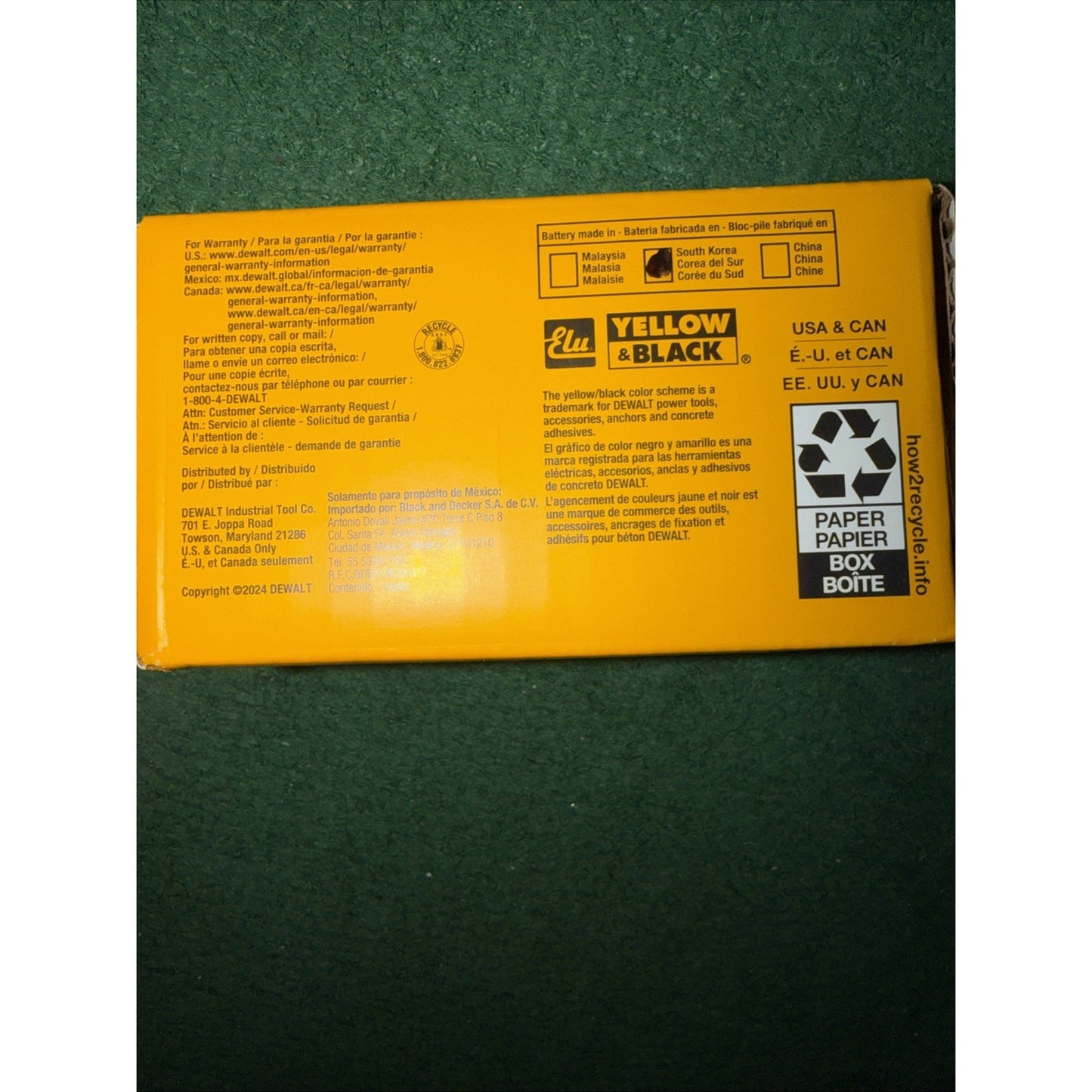 Yellow cardboard packaging showing warranty information, manufacturer contact details, recycling instructions, and a "Yellow & Black" trademark logo on a green textured surface.