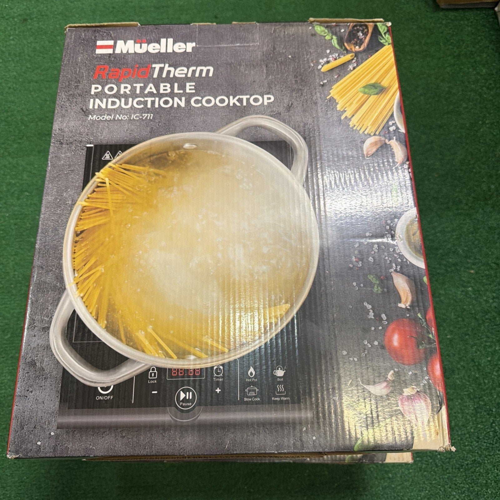 Box packaging for a Mueller RapidTherm portable induction cooktop showing the device with a boiling pot of spaghetti and ingredients like tomatoes, garlic, and herbs on a dark background.