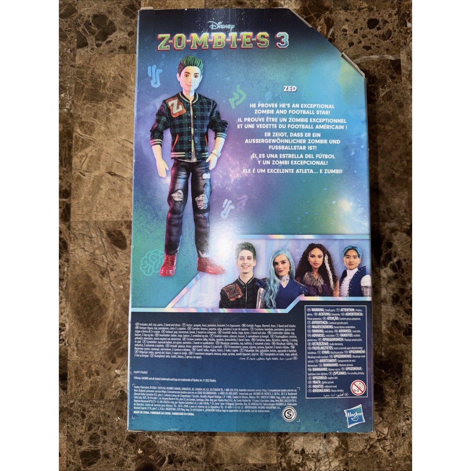Packaging backing card for a Disney Zombies 3 Zed action figure, showing an illustration of Zed in casual attire with green hair, a description in multiple languages, and images of four characters at the bottom.