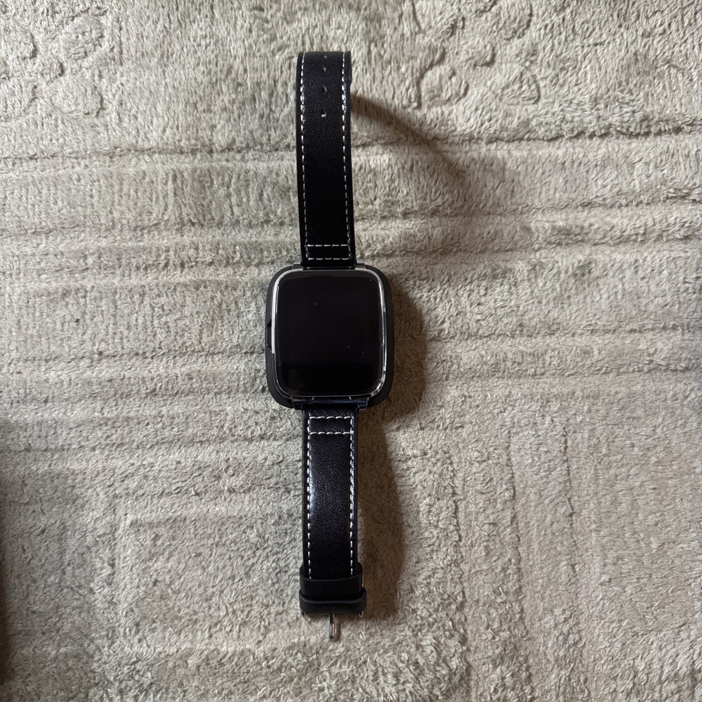 Bit Smart Watch Model S1 with black leather band and rectangular display shown lying flat on textured surface