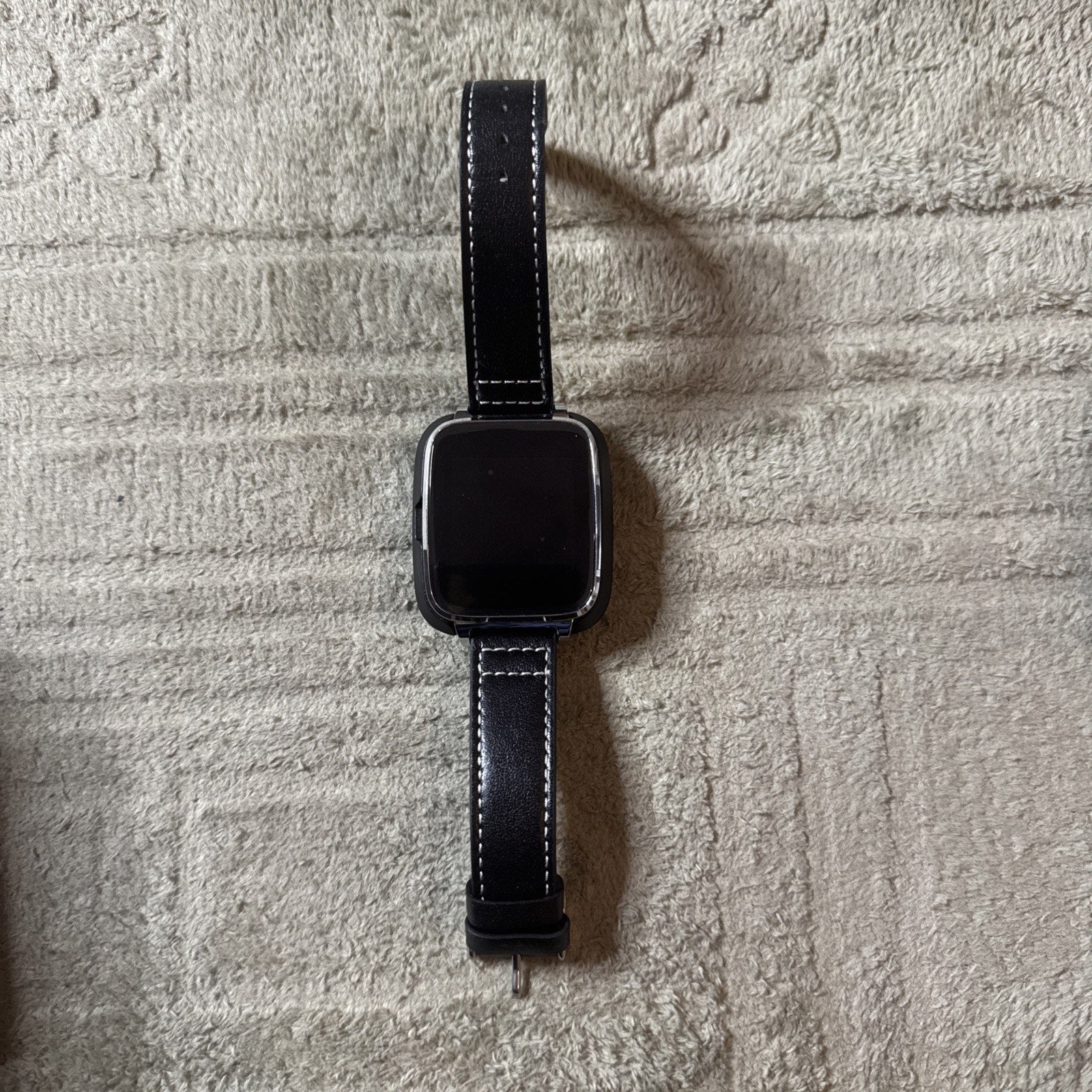 Bit Smart Watch Model S1 with black leather band and rectangular display shown lying flat on textured surface