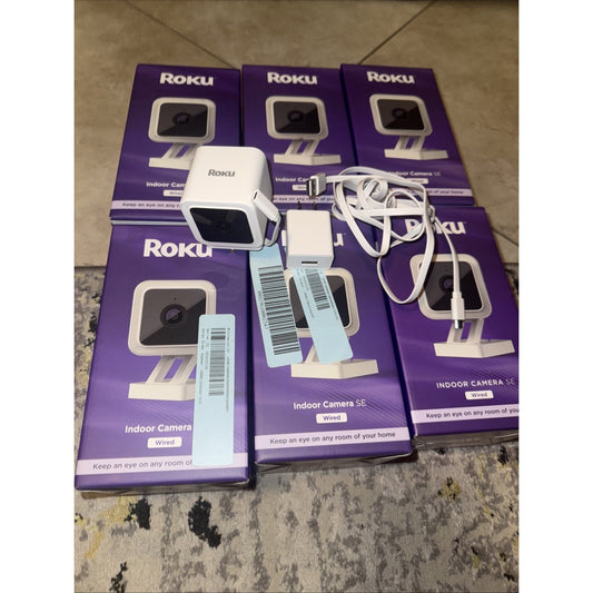 Lot of 6 Roku Smart Home Indoor Camera SE Wi-Fi with white wired cameras and purple packaging boxes displayed on floor