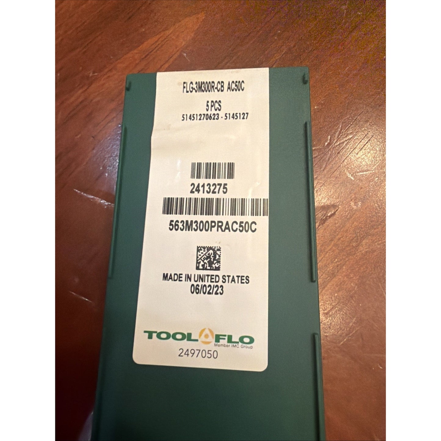 Dark green rectangular container with a white label displaying product code "FLGAK30DR-CB AC30C," quantity "5 PCS," barcodes, manufacturing date "06/02/23," and "Made in United States," placed on a wooden surface.
