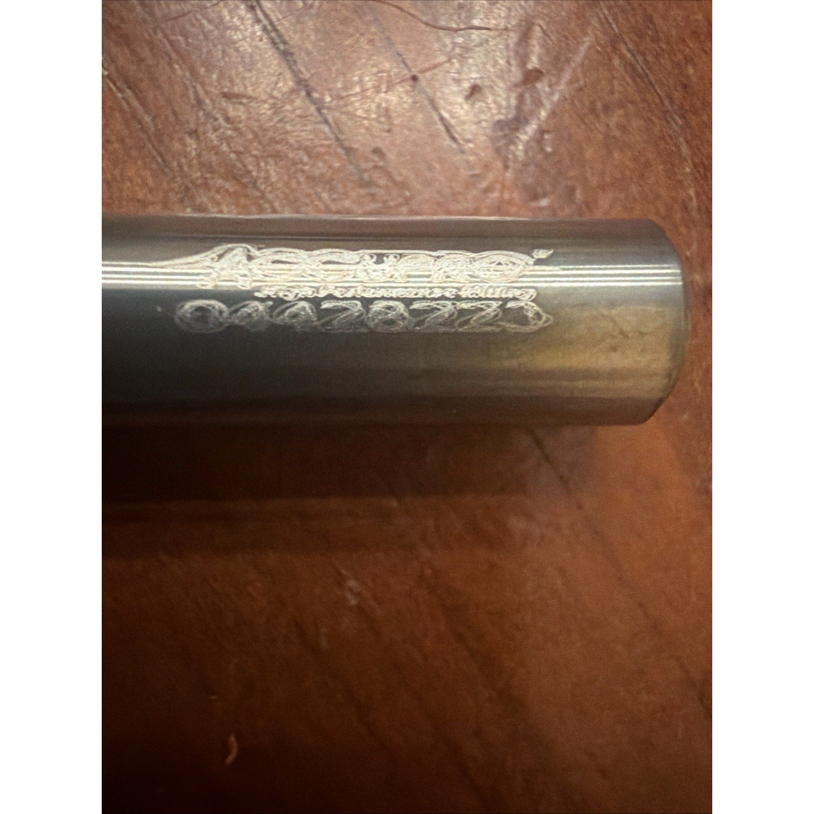 Close-up of a polished metal tool shaft with partially worn engraved numbers and letters, placed on a textured wooden surface.