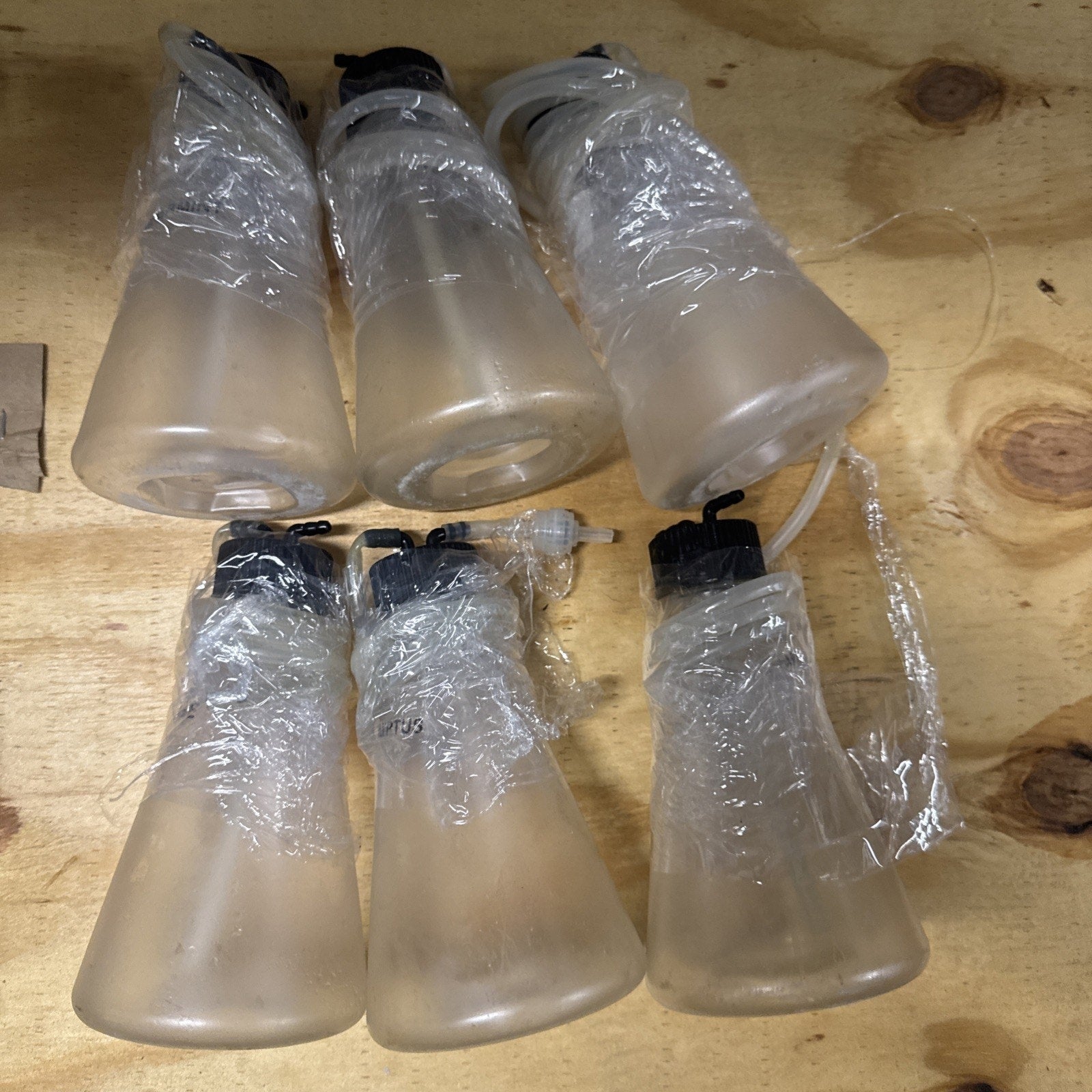 Set of six translucent oxygen bar scent bottles wrapped in plastic with black caps and attached tubing on wooden surface