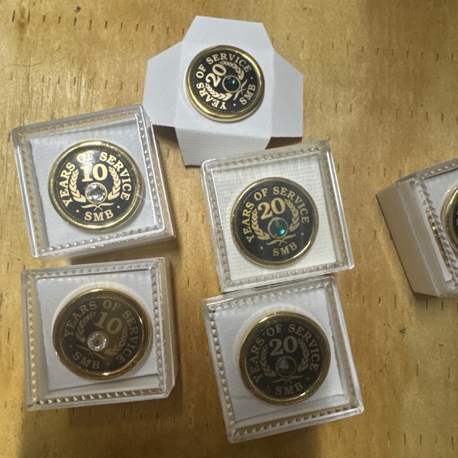 Set of 8 gold tone employee award pins showing 10, 20, and 45 years of service with SMB logo on wooden surface