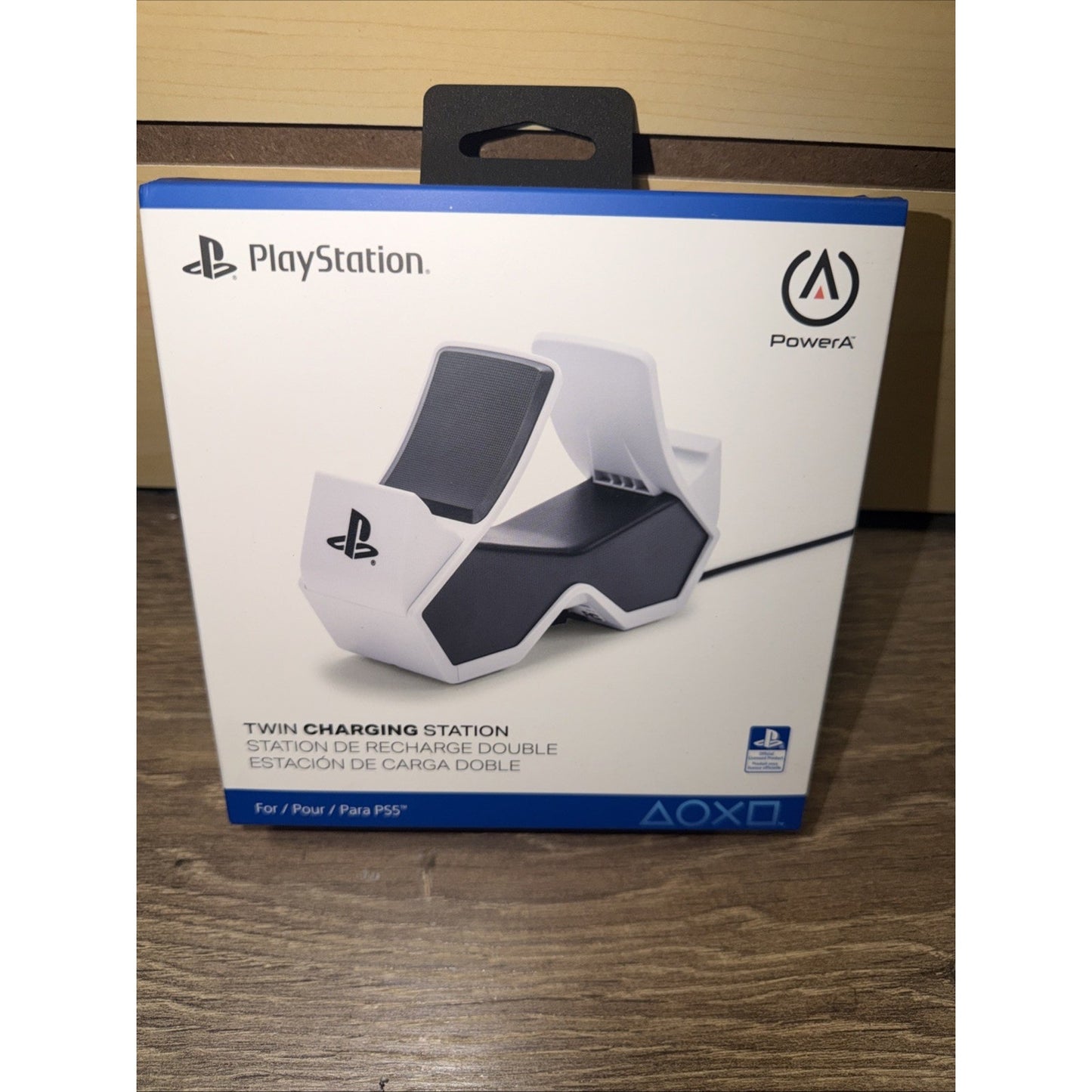 Packaging of a PlayStation twin charging station for PS5 controllers by PowerA, showing the white and black charging dock on a wooden surface.