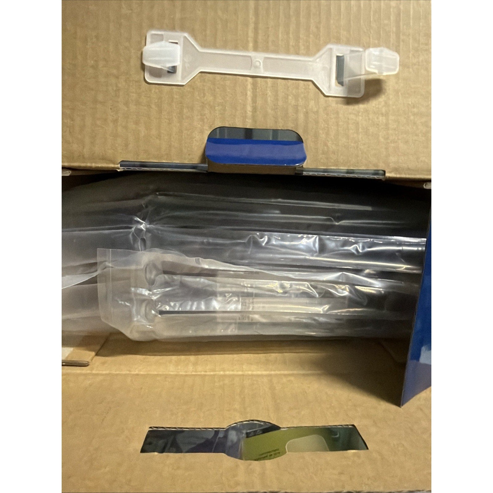 Open cardboard box containing clear inflatable air cushion packaging for product protection, with a white plastic securing clip visible on the box flap.