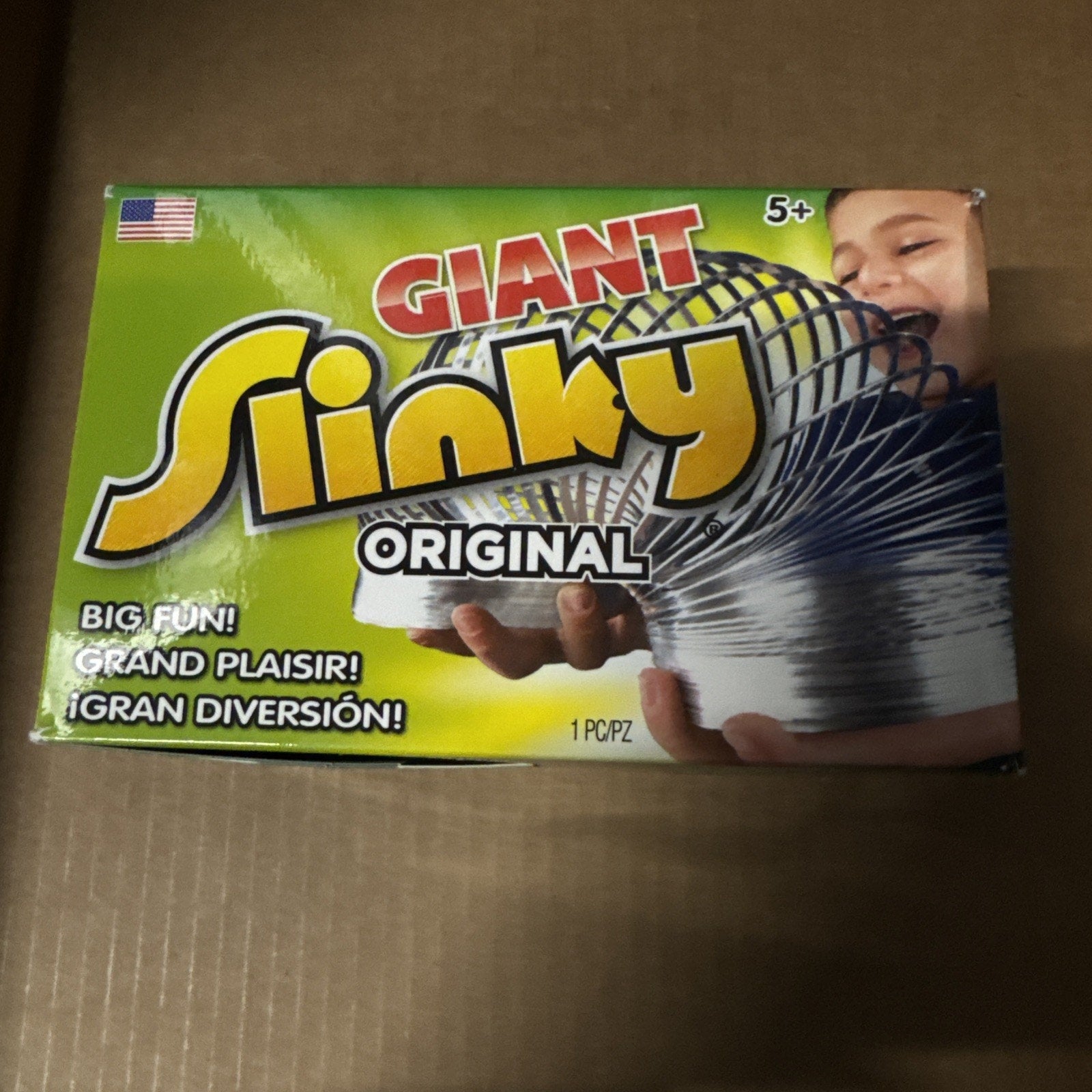 The Original Giant Slinky Walking Spring Toy box showing colorful logo and child playing with large metal slinky age 5+