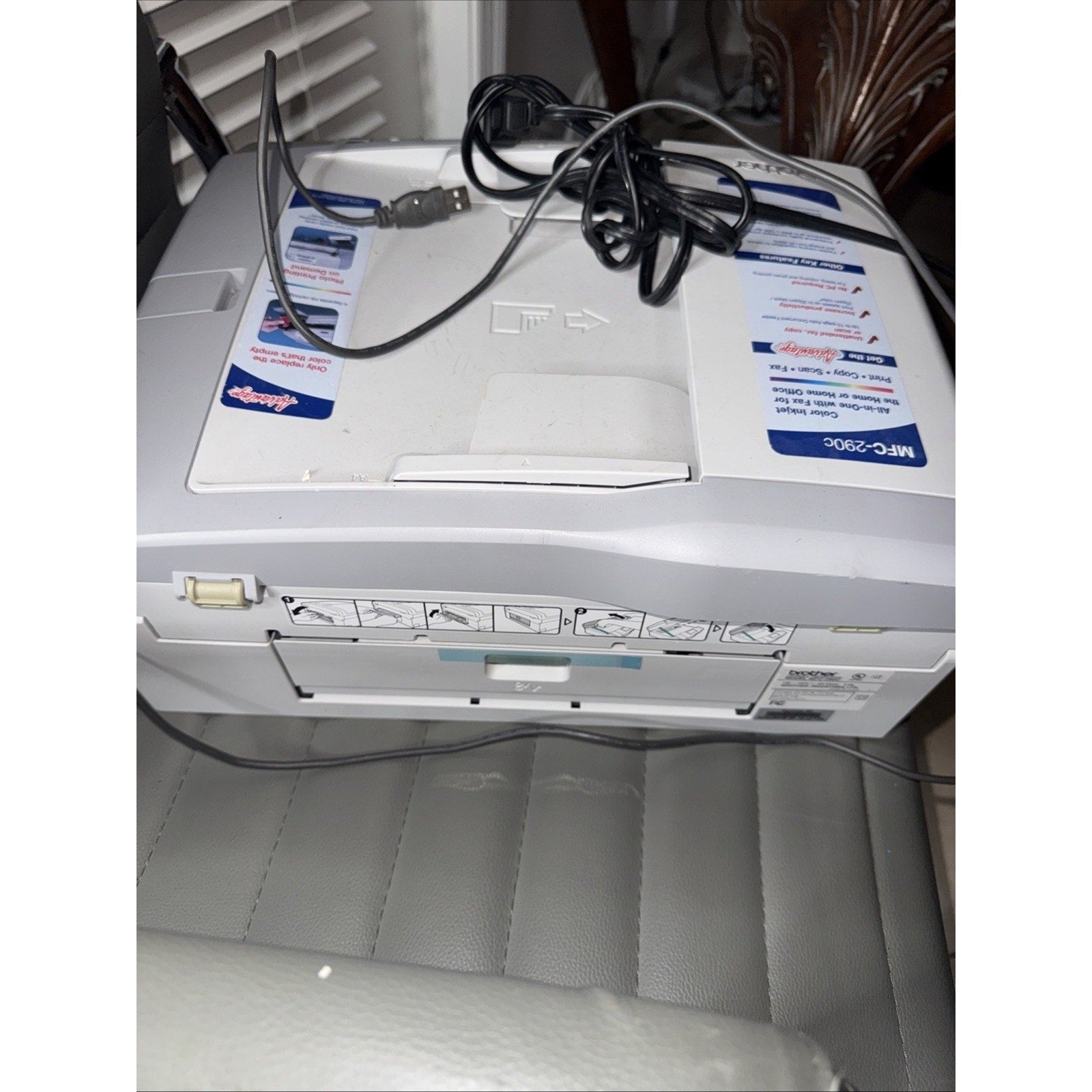 Brother MFC-290C All-In-One Inkjet Printer with USB cable on top shown from front on gray leather surface and chair background