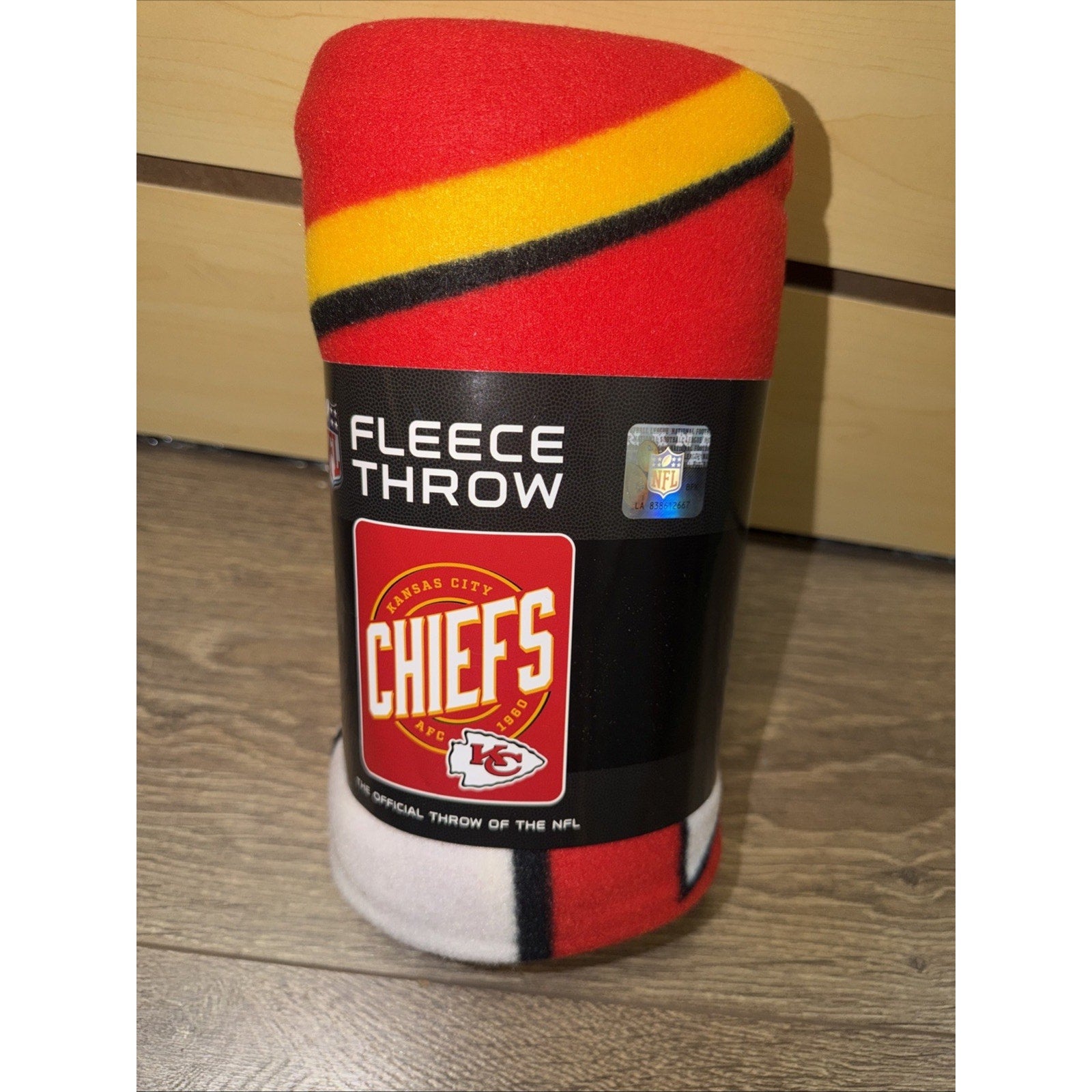 Rolled fleece throw blanket wrapped in black packaging featuring the Kansas City Chiefs logo, with visible red, yellow, black, and white colors on the fabric.
