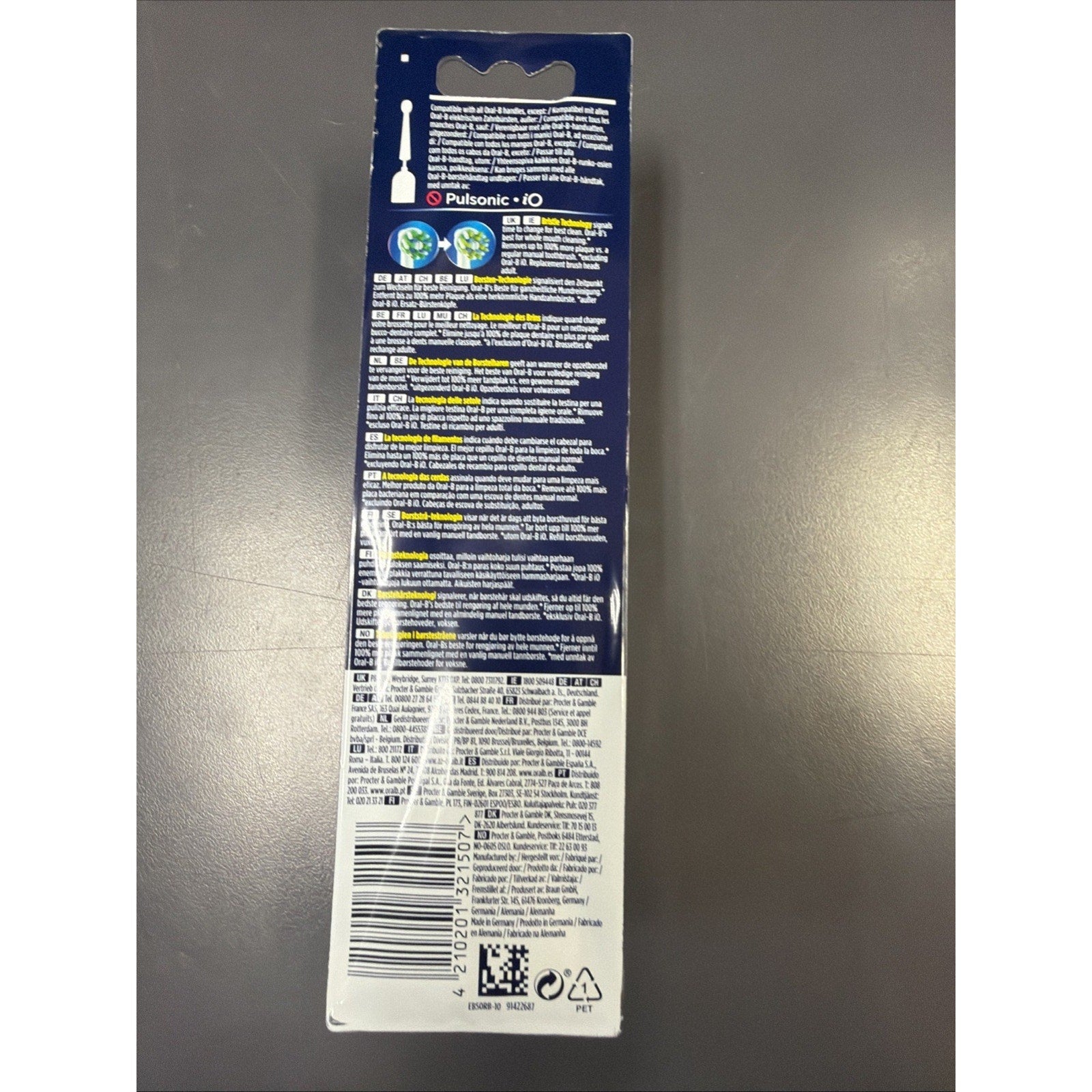 Tall rectangular blue and white cardboard package displaying multilingual product instructions, safety information, and a barcode at the bottom, photographed on a gray surface.