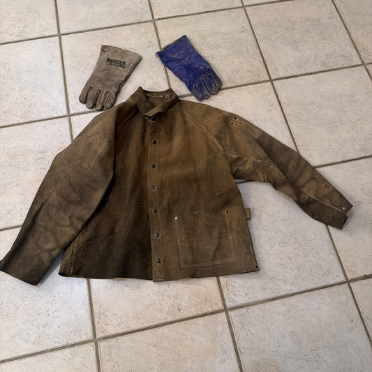 Heavy-duty leather welding jacket coat with snap buttons and matching protective welding gloves laid flat on tile floor