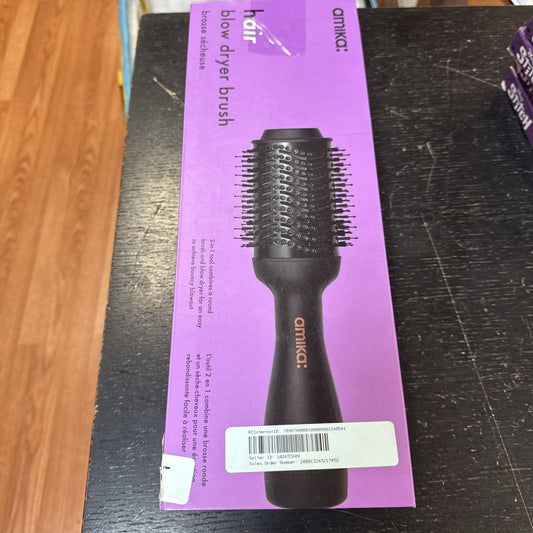 Amika Hair Blow Dryer Brush in black with round bristles displayed on purple packaging box on wooden surface
