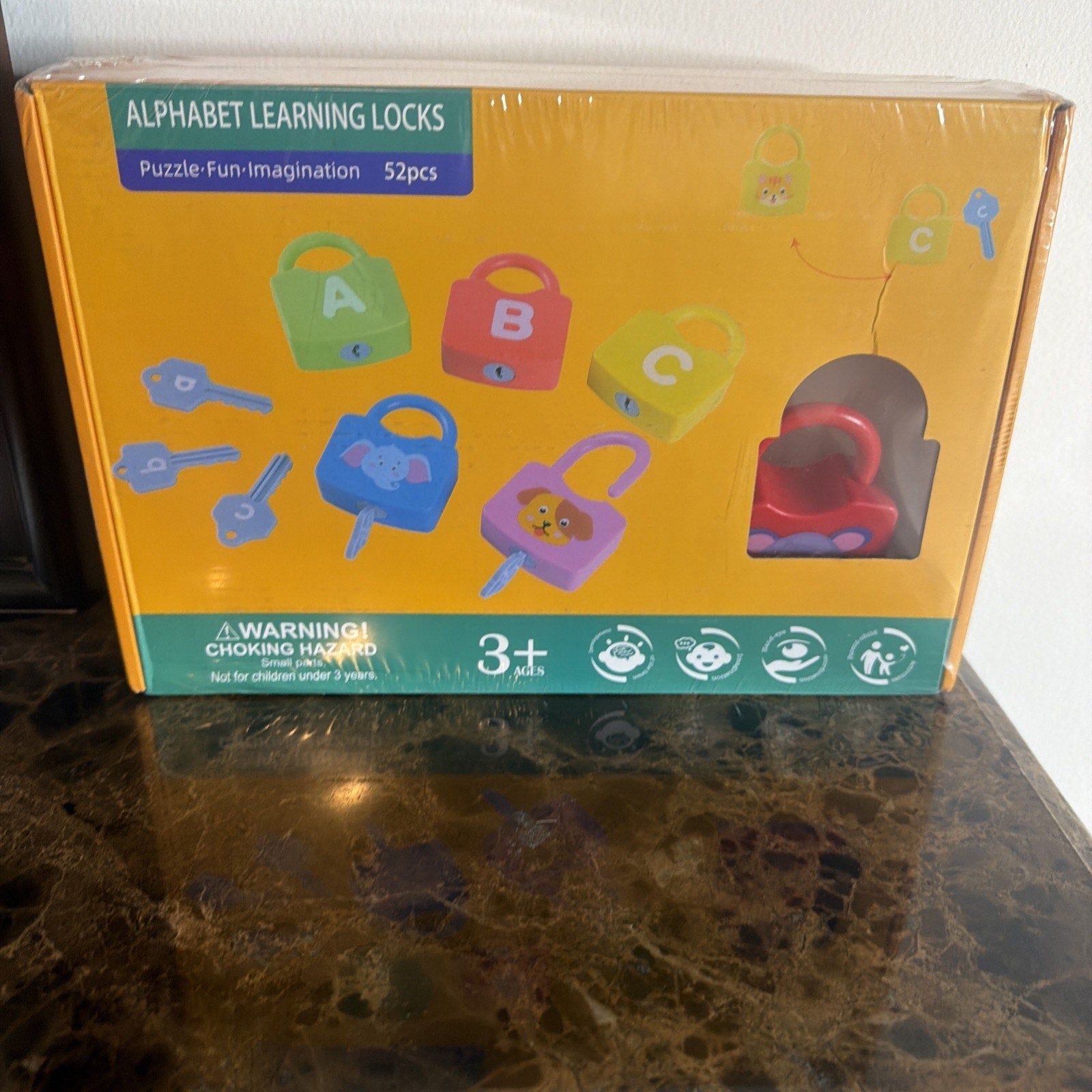 Colorful educational toy set featuring plastic alphabet-themed locks and matching keys designed to teach young children letters and unlock skills, packaged in a yellow box with a clear window showing a red lock inside.