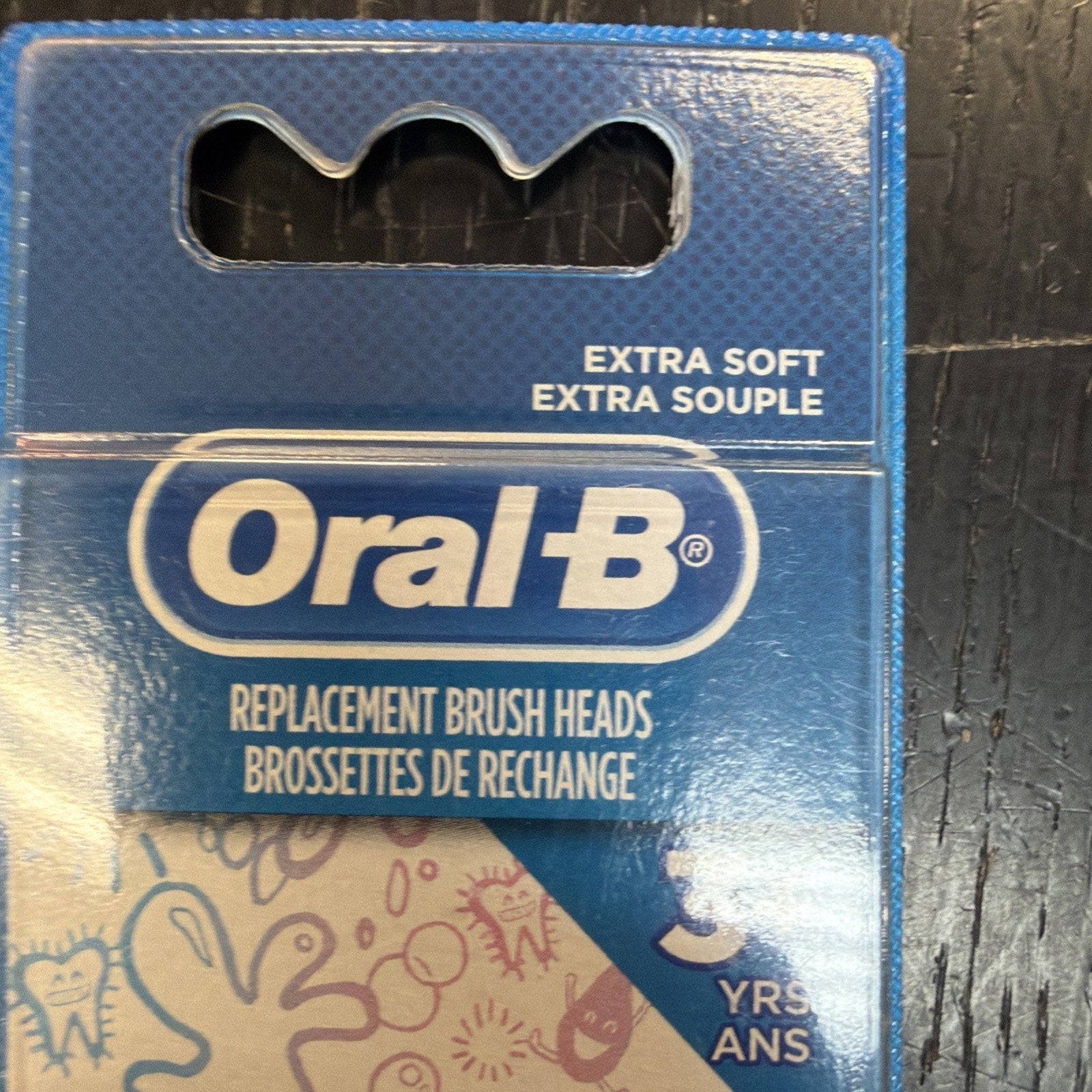 Close-up of blue Oral-B replacement brush heads packaging highlighting the "extra soft" label and partial decorative illustrations visible beneath the brand name.