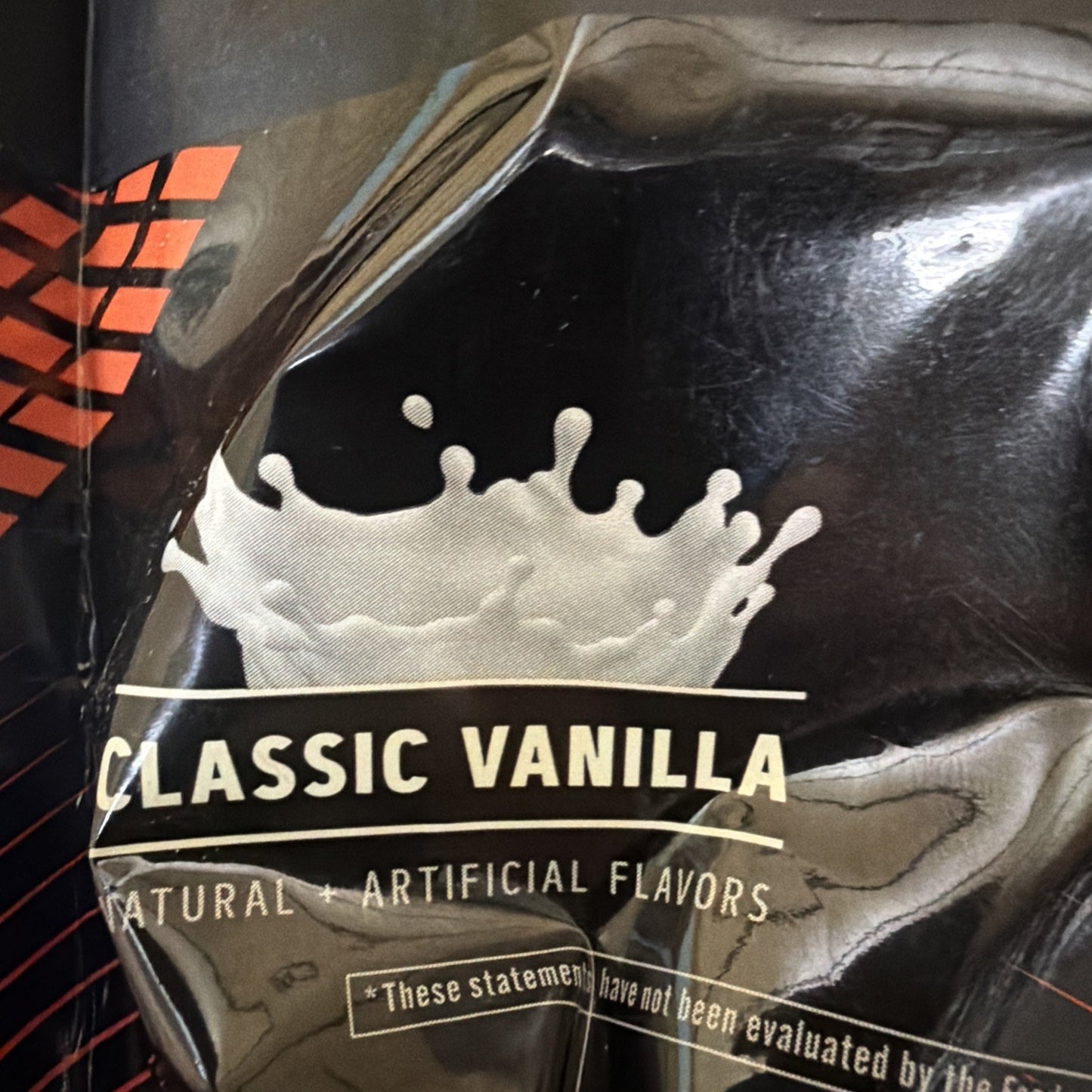 Close-up of black packaging featuring a milk splash graphic and text indicating classic vanilla flavor with natural and artificial flavors.