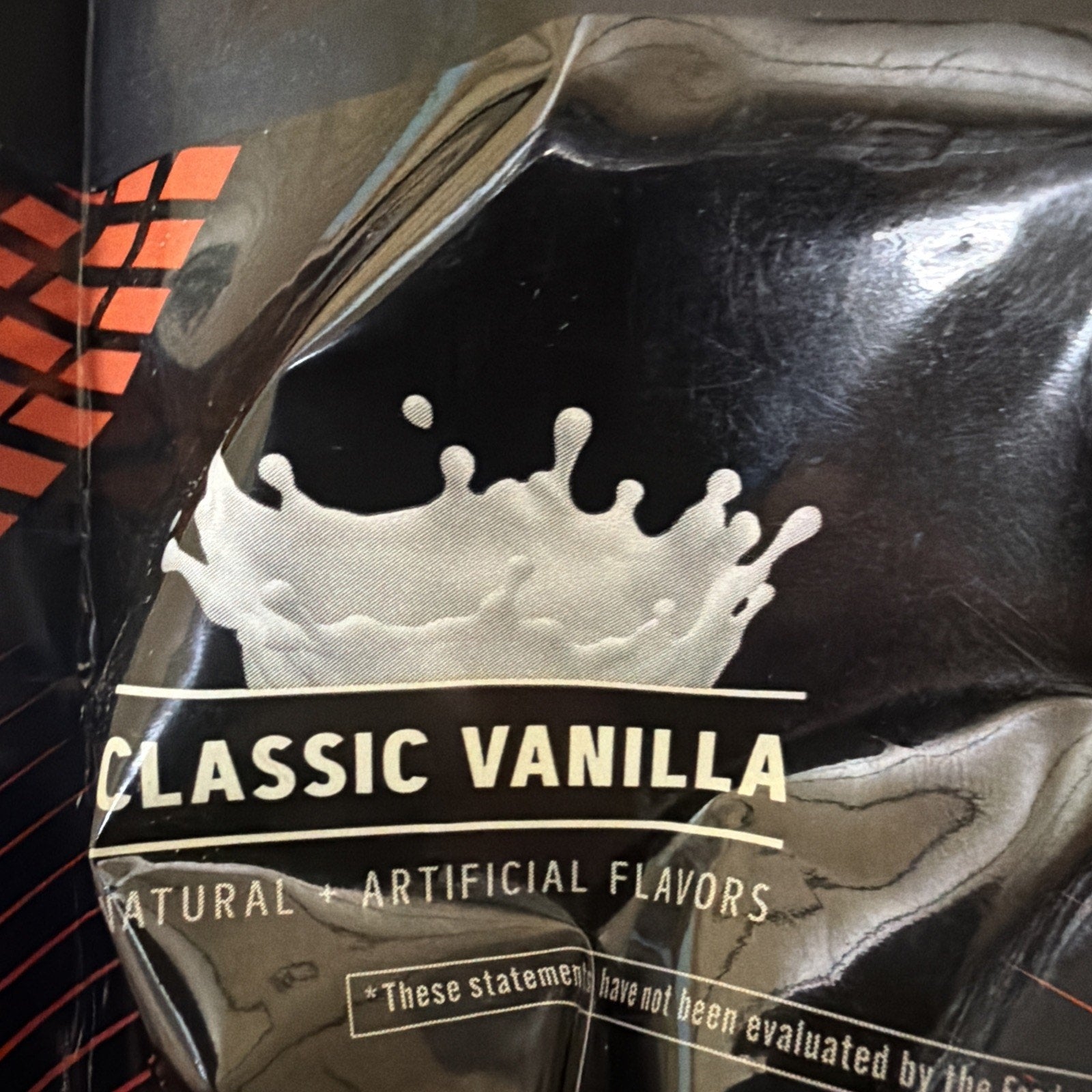 Close-up of black packaging featuring a milk splash graphic and text indicating classic vanilla flavor with natural and artificial flavors.