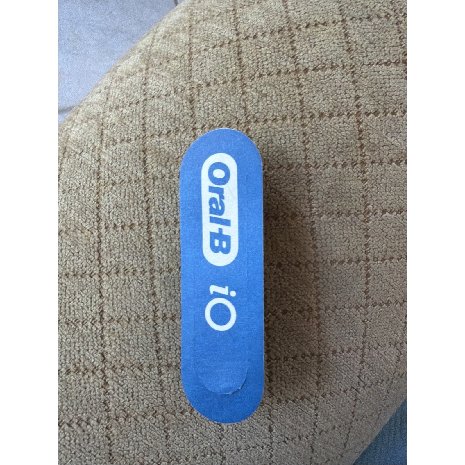 Top view of blue Oral-B iO Series toothbrush replacement brush head package on textured brown fabric background