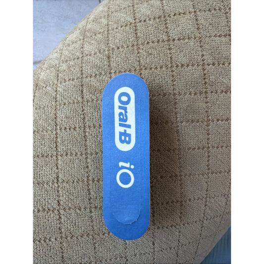 Top view of blue Oral-B iO Series toothbrush replacement brush head package on textured brown fabric background