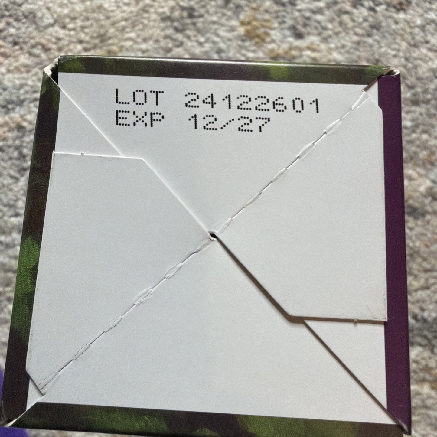 Close-up of the bottom of a folded cardboard box showing the lot number 24122601 and expiration date 12/27 printed in black ink.