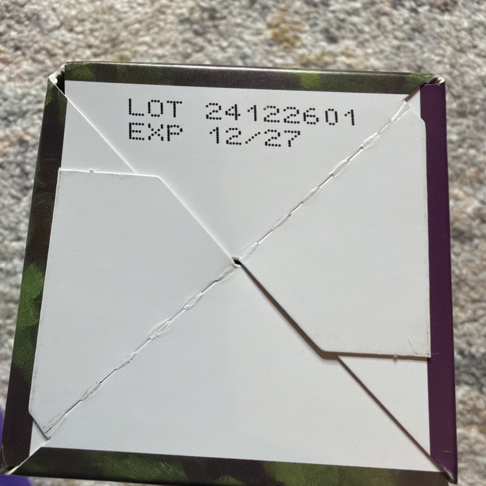 Close-up of the bottom of a folded cardboard box showing the lot number 24122601 and expiration date 12/27 printed in black ink.