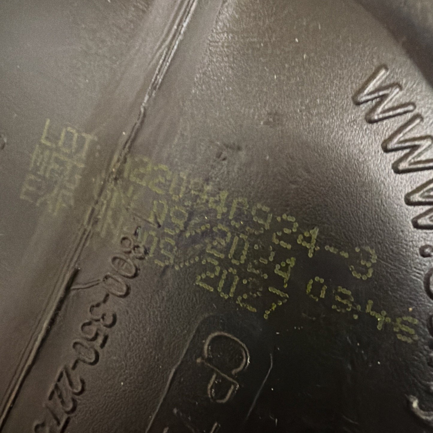 Close-up of a manufacturing stamp on a black plastic surface showing a lot number, manufacturing date, and expiration date printed in faded yellow ink.