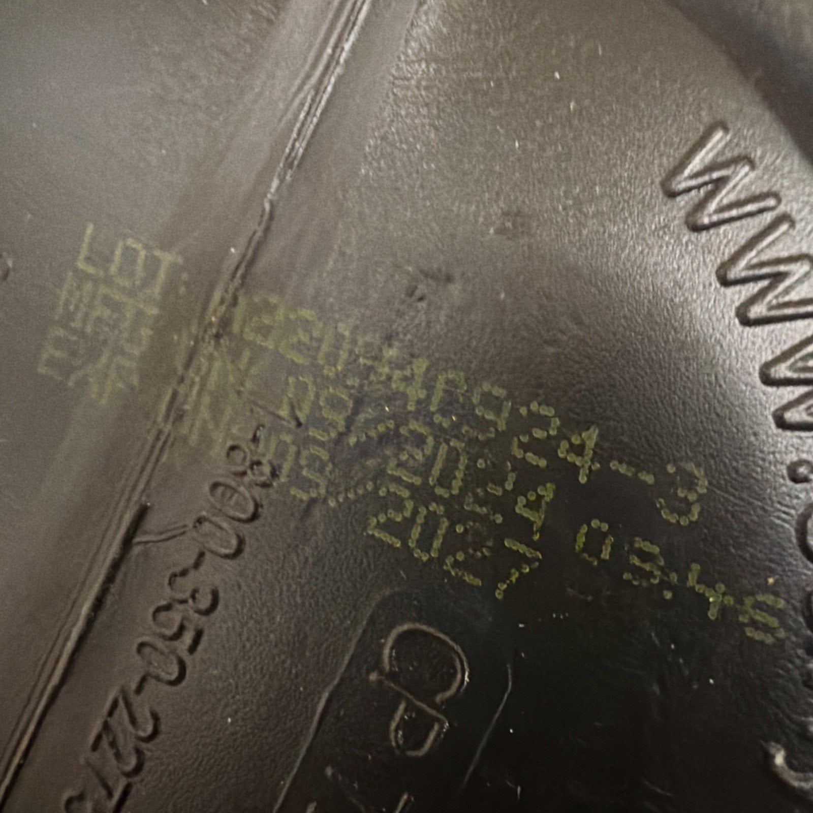 Close-up of a manufacturing stamp on a black plastic surface showing a lot number, manufacturing date, and expiration date printed in faded yellow ink.