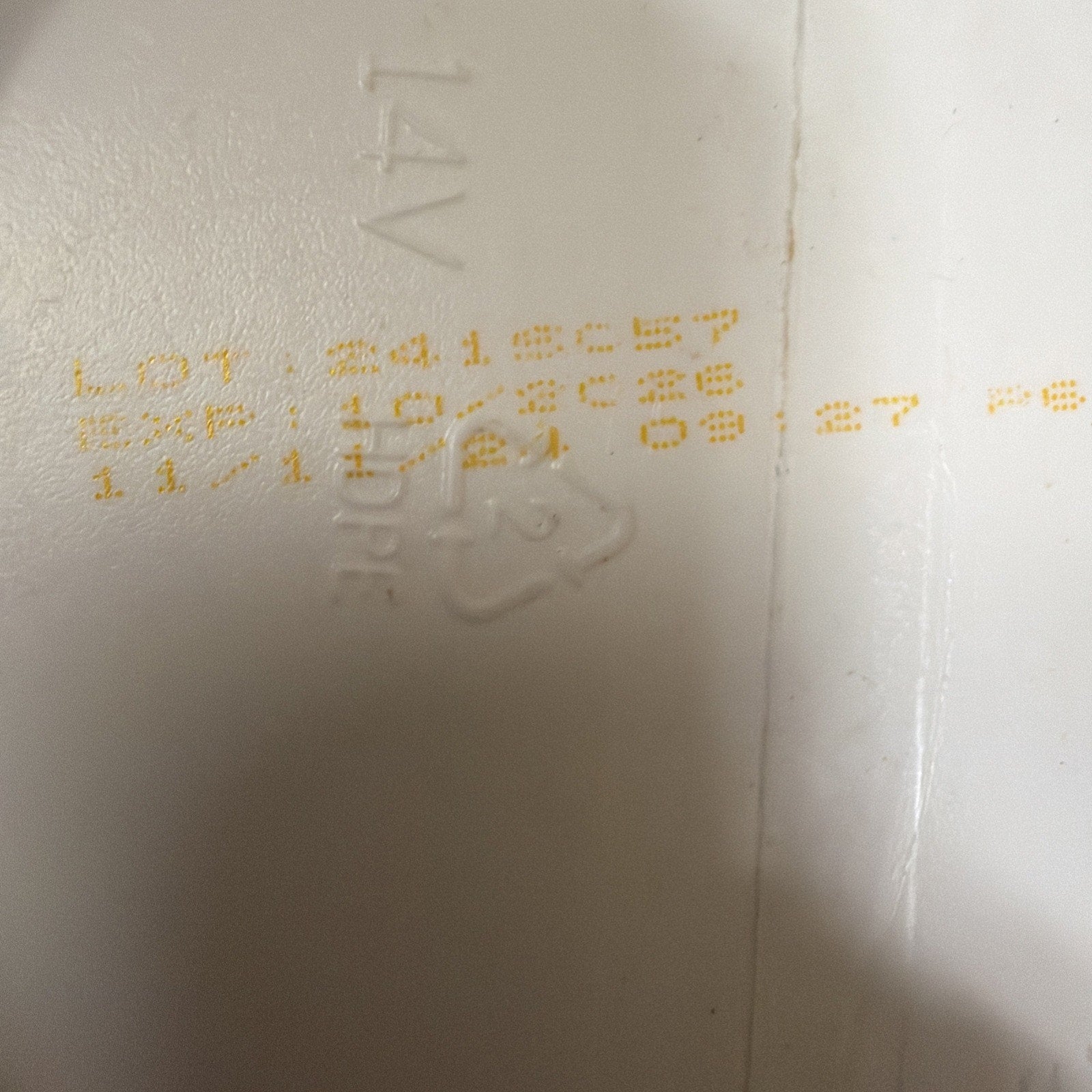 Close-up of yellow printed batch number, expiration date, and time code on a white plastic surface with embossed recycling symbol and the text "14V" and "HDPE.
