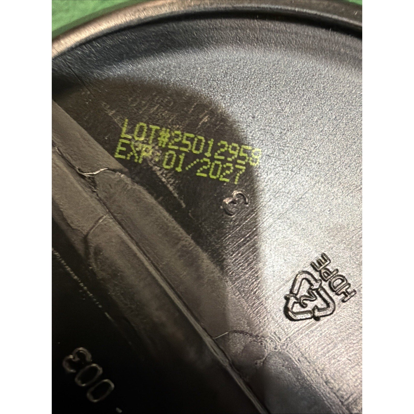 Close-up of a black plastic container lid showing a yellow printed lot number and expiration date, with a recycling symbol indicating HDPE material.