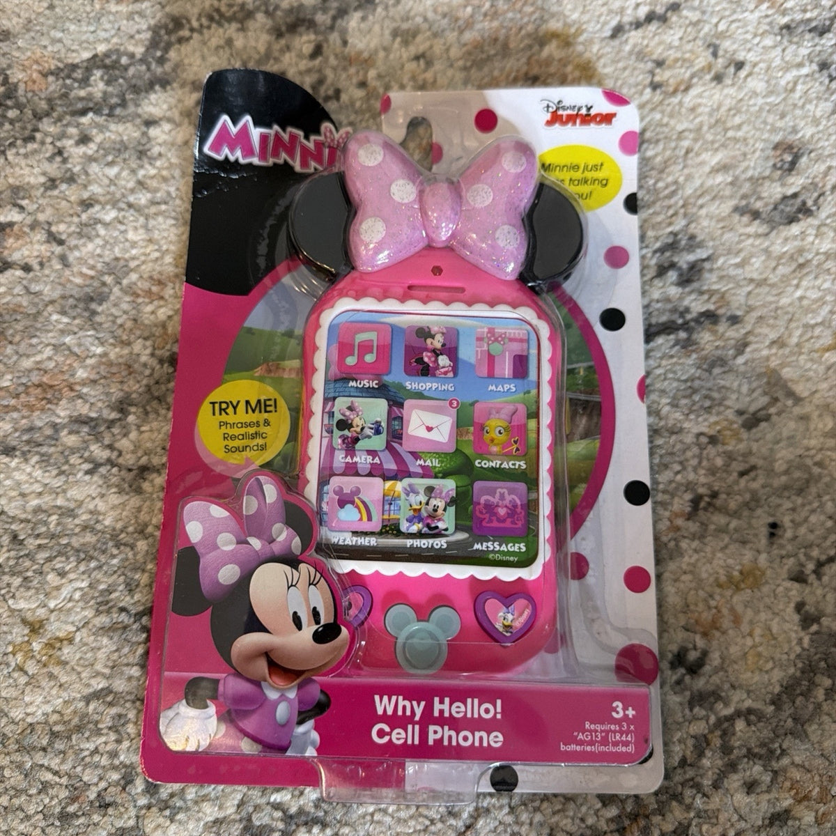 Pink Minnie Mouse themed toy cell phone with a large pink bow on top, featuring colorful app icons on the screen and packaged in a pink and white polka dot blister card with a cartoon Minnie illustration.