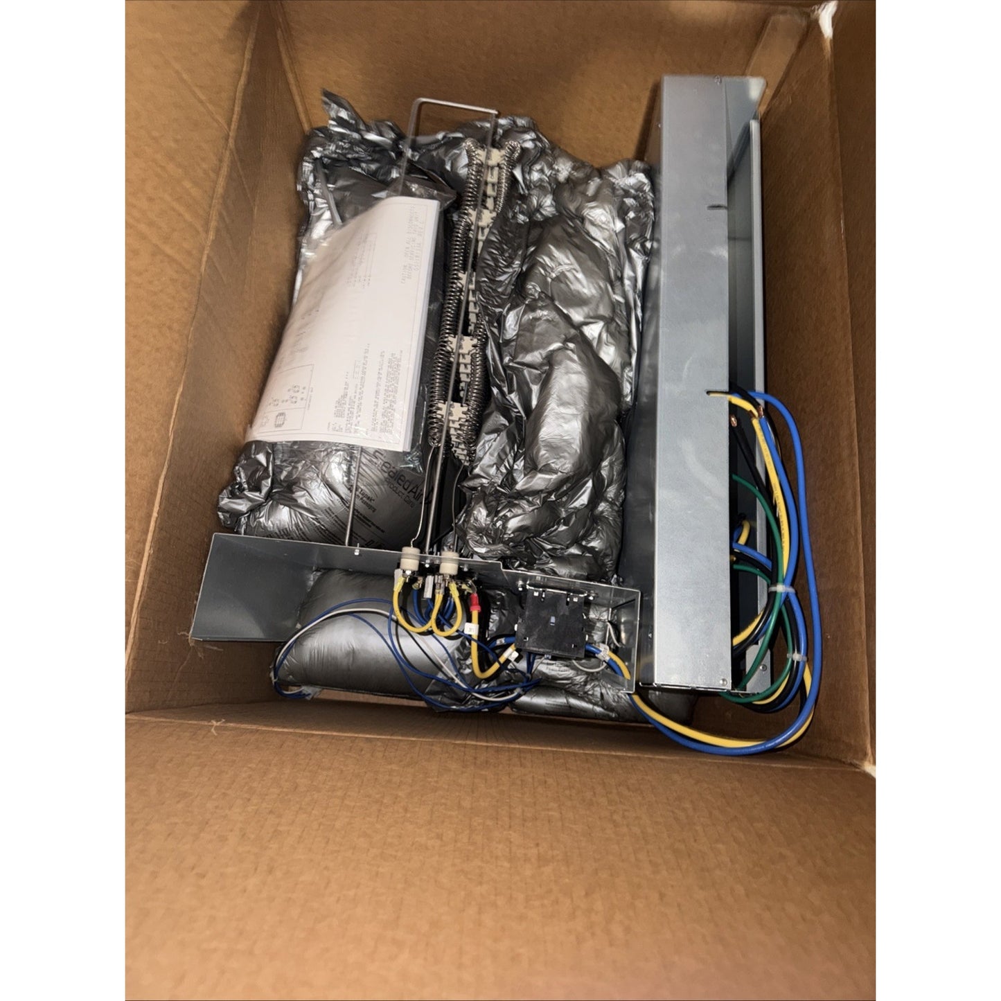 Metal heating element assembly with metal coils, wiring, and insulation materials packed inside a brown cardboard box.