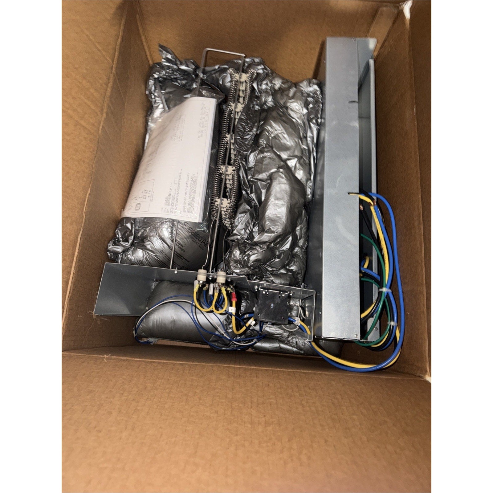 Metal heating element assembly with metal coils, wiring, and insulation materials packed inside a brown cardboard box.