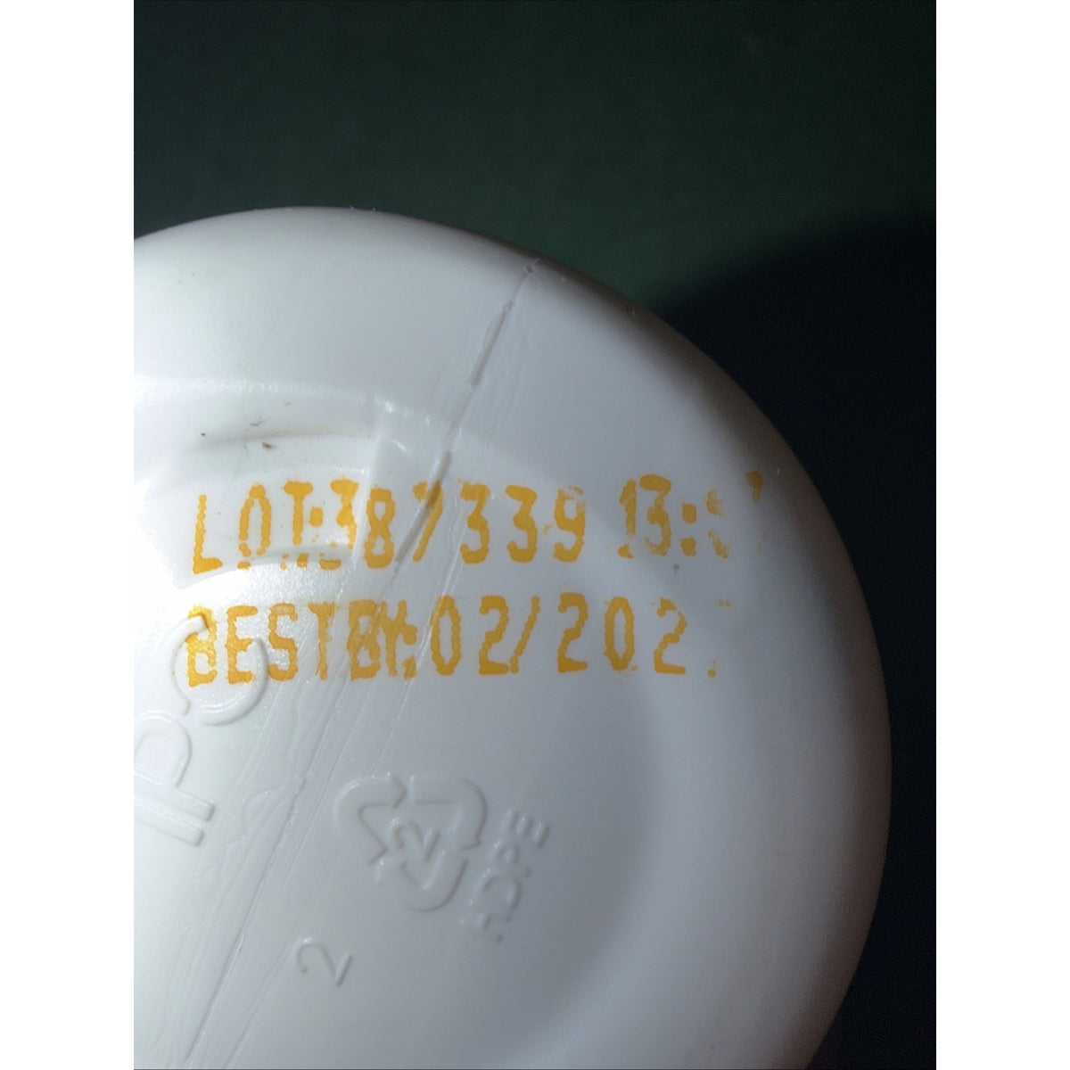 Close-up of a white plastic container bottom showing a partially visible yellow lot number and a best before date printed on the surface.