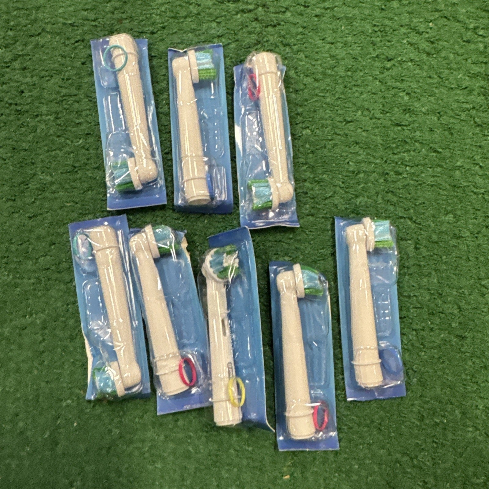 Pack of 8 Oral B Precision Clean replacement electric toothbrush heads in individual sealed blue packaging on green surface
