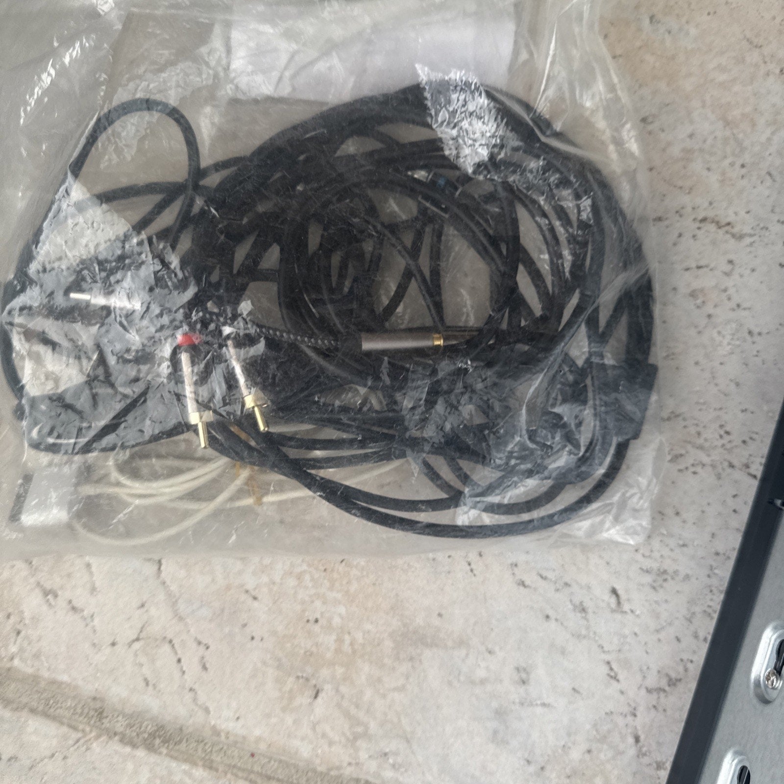 Plastic bag containing various black and white audio and video cables with connectors on tile floor