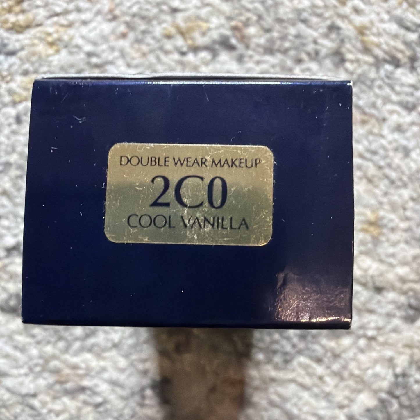 Close-up of a navy blue makeup box with a gold label showing the shade "2C0 Cool Vanilla" for Double Wear Makeup.